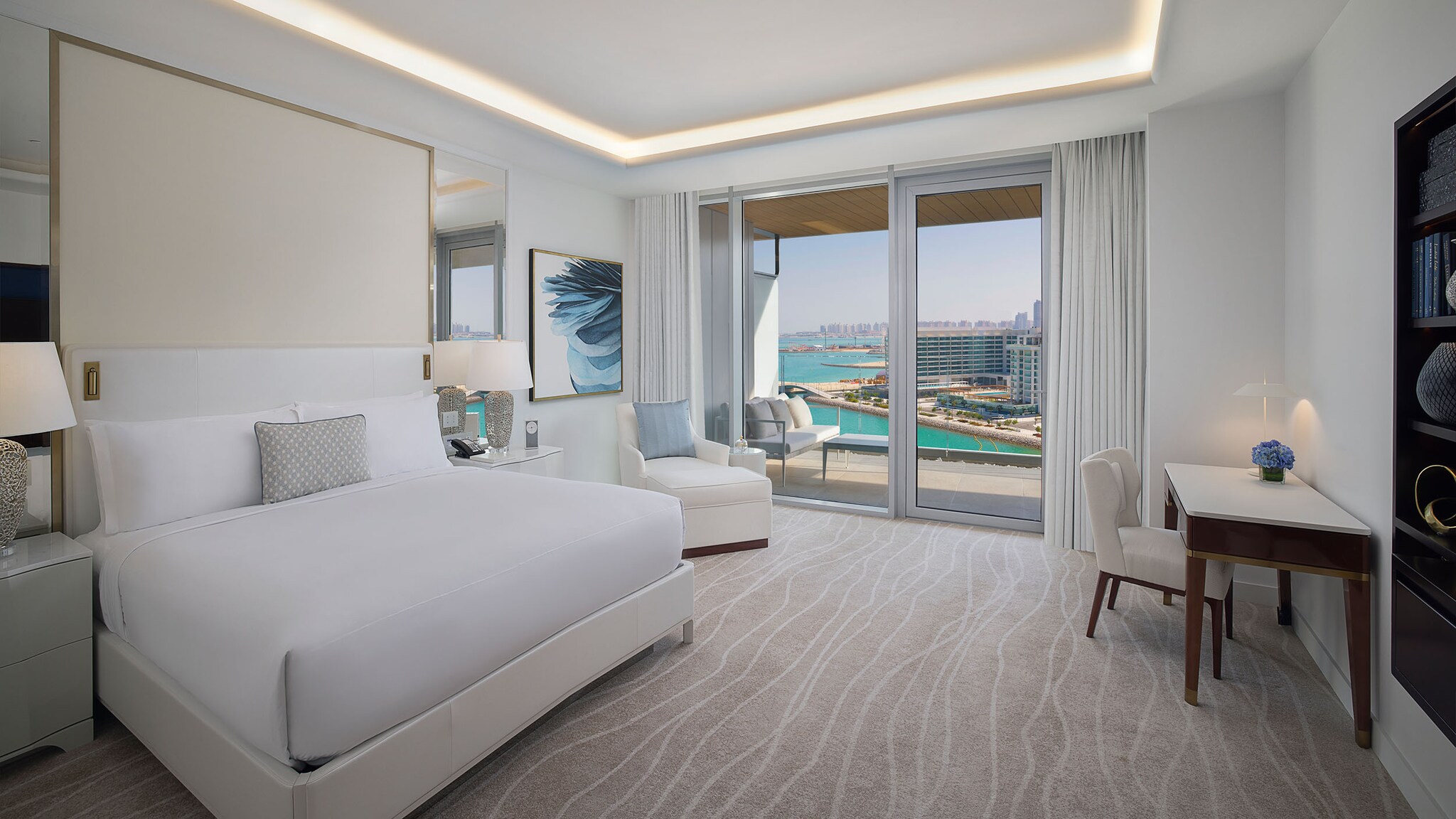 Ein großes Doppelbett steht in einem Hotelzimmer, mit einer Terrassentür mit Blick auf das Meer.