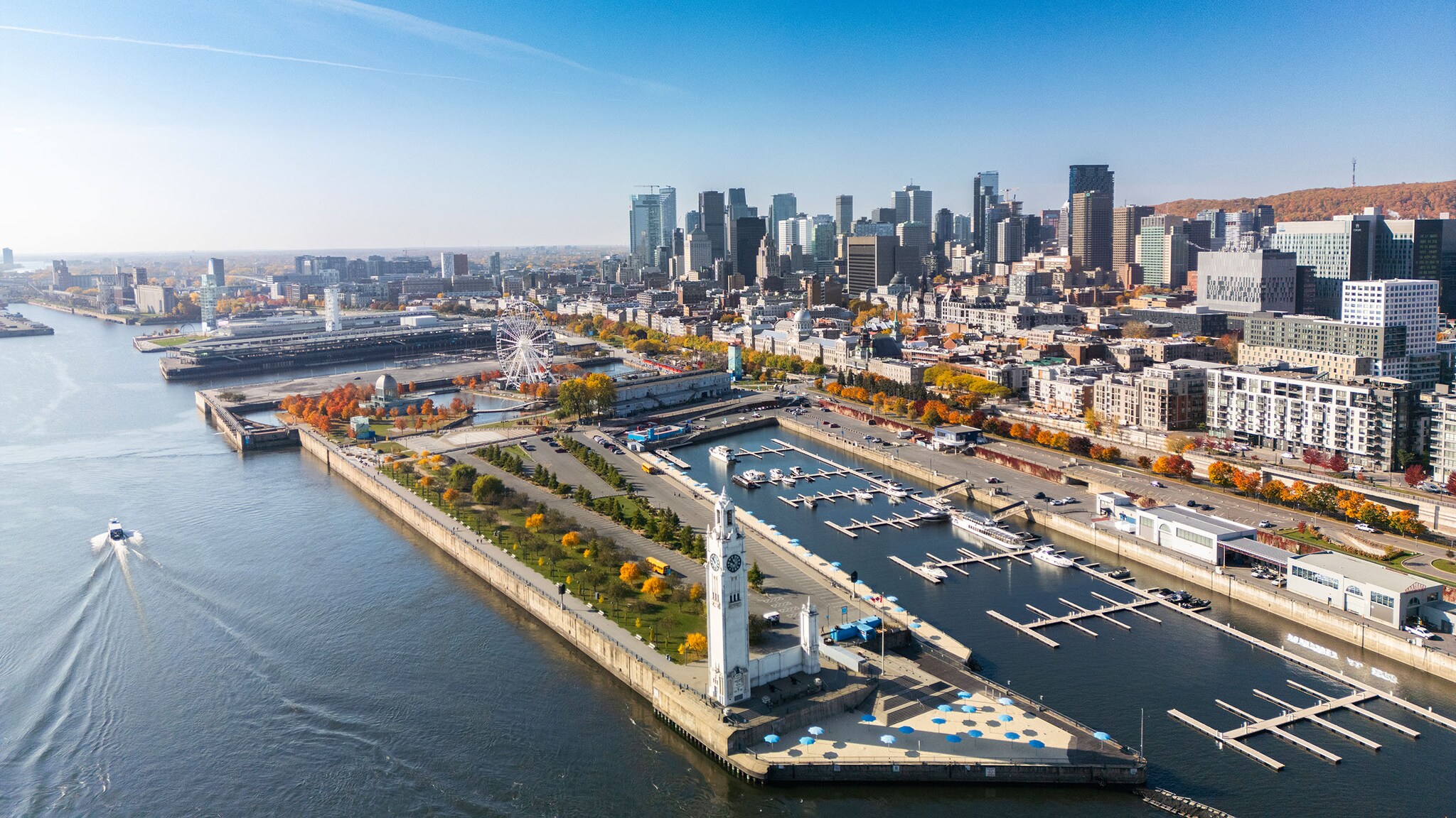 Luftaufnahme der Skyline von Montréal am Wasser mit Promenade, Riesenrad und Hafenbecken.