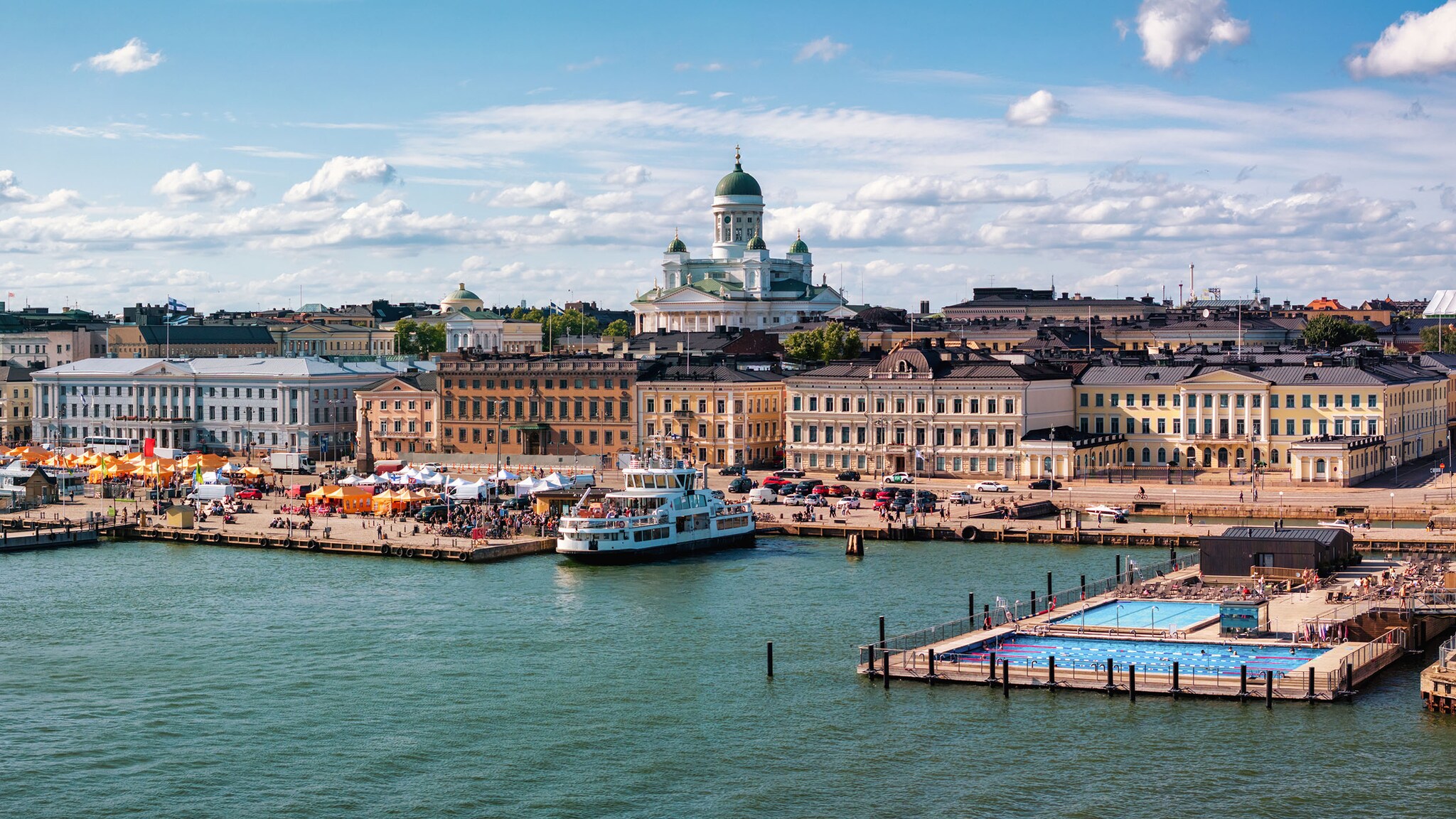 Stadtpanorama von Helsinki mit Hafenpromemnade und Schwimmbecken im Wasser.