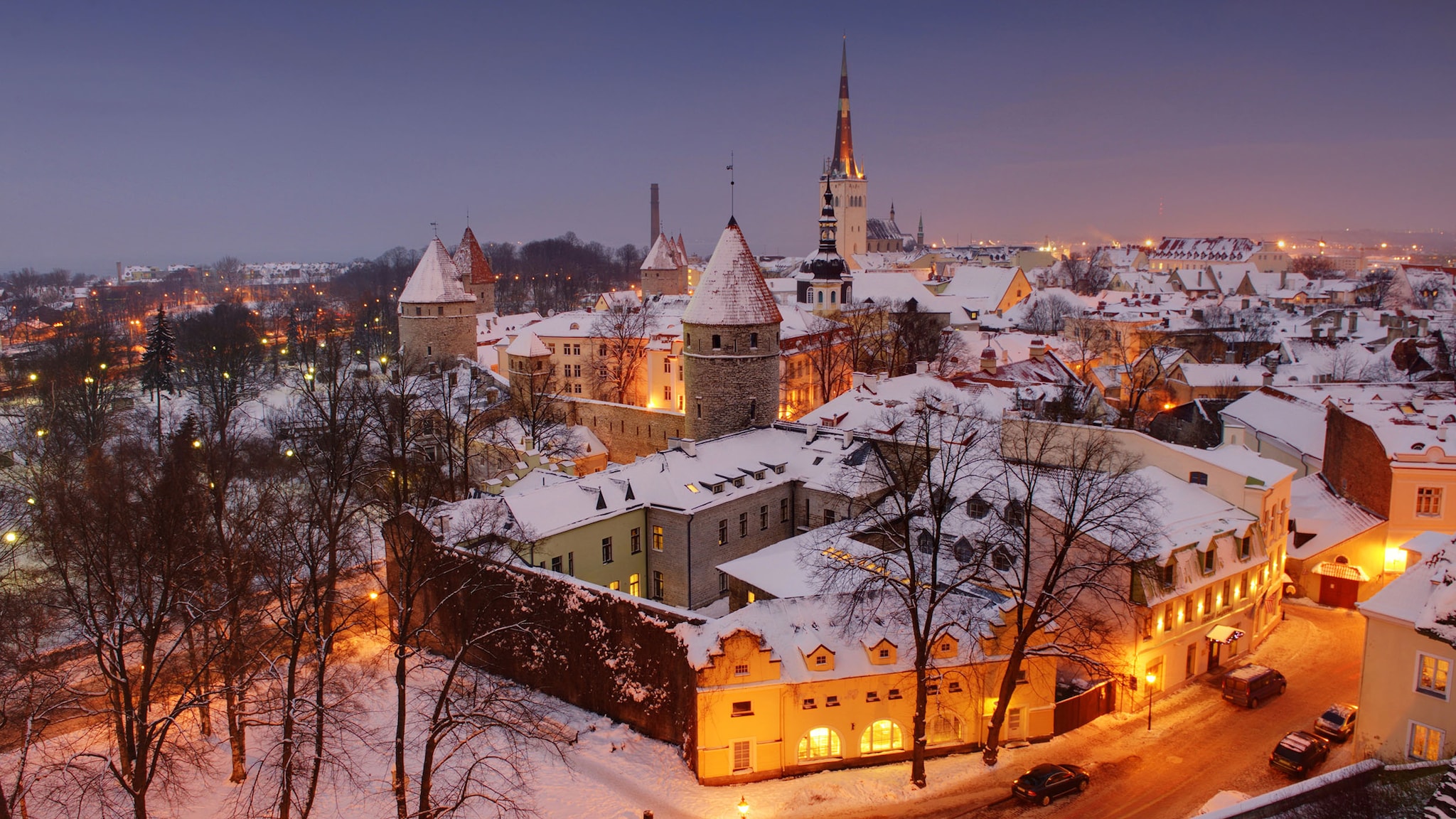 Mittelalterliche Altstadt von Tallinn mit beleuchteten Häusern und schneebedeckten Dächern bei Abenddämmerung.