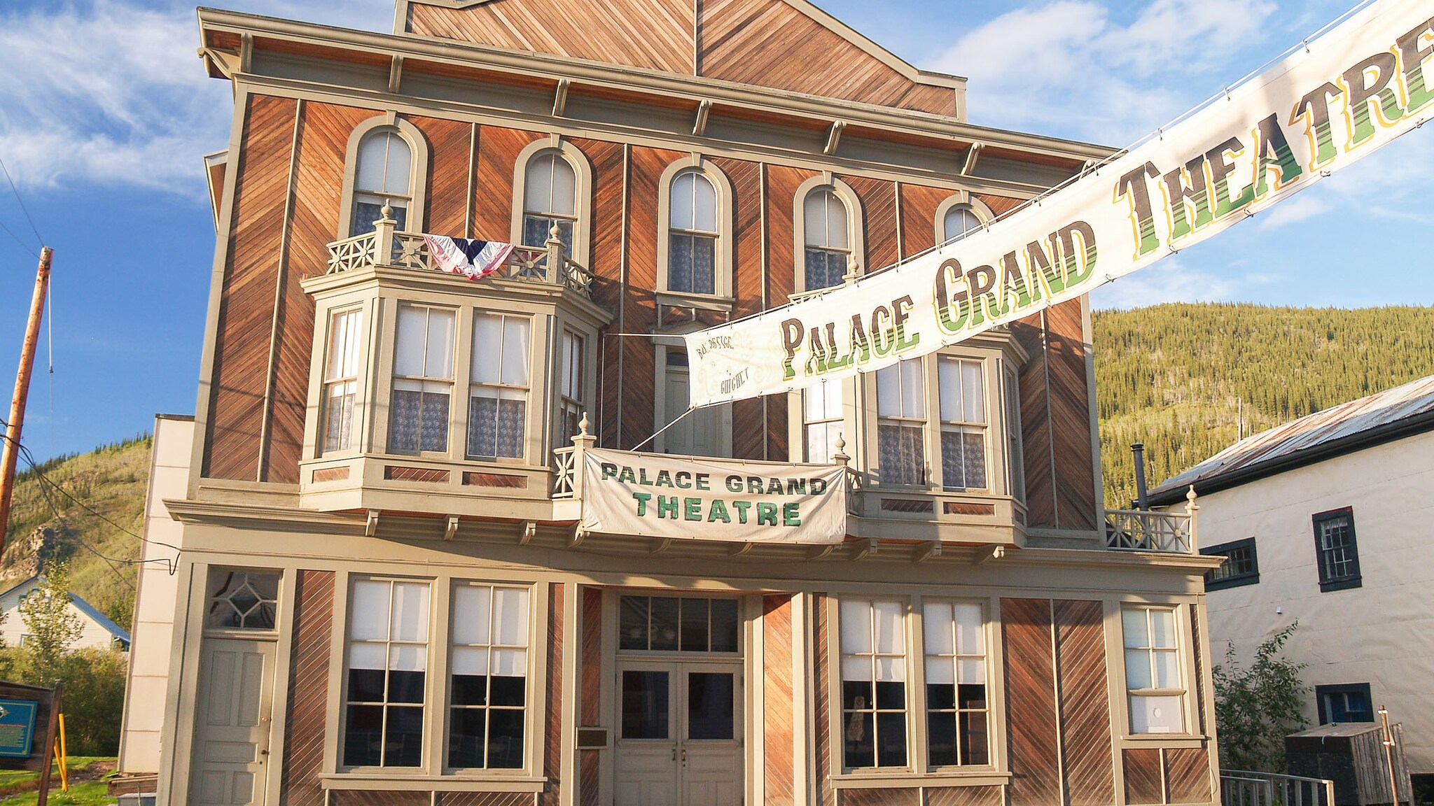 Fassade eines historischen Theatergebäudes aus Holz im Boomtown-Stil mit einem davor gespannten Banner.