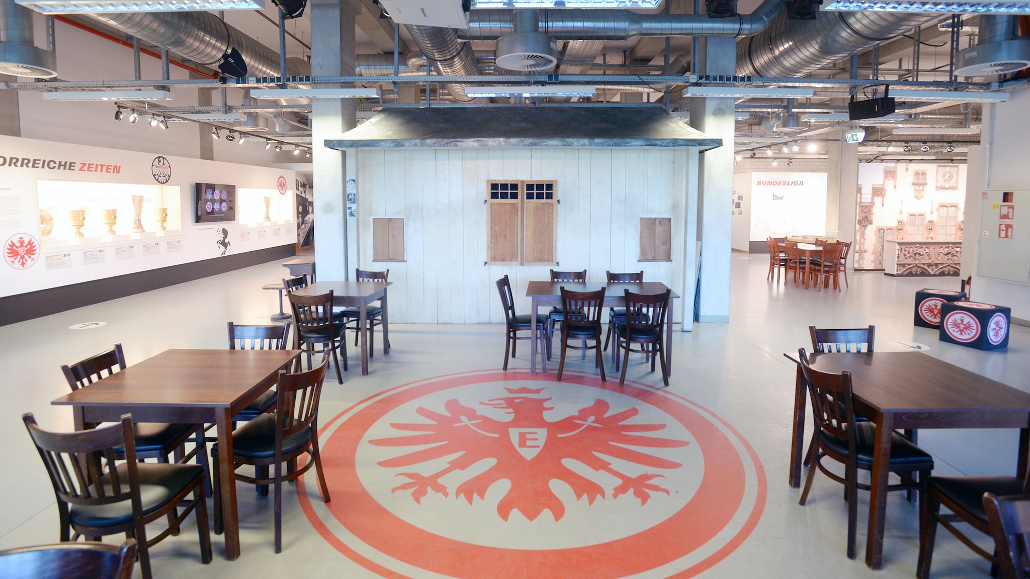Ausstellungsraum mit Tischen um ein rundes, rotes Adlerwappen auf dem Boden.