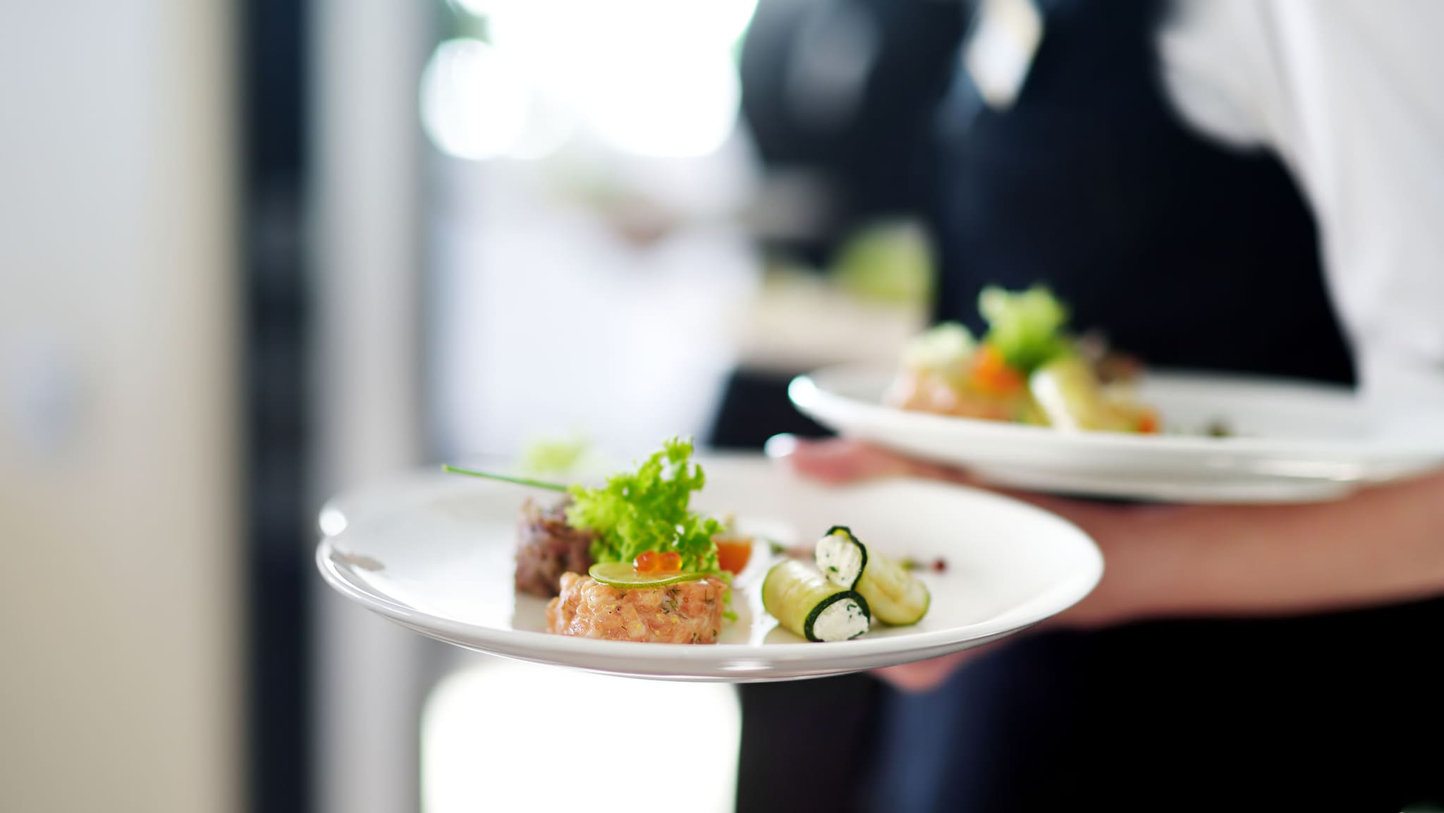 Ein Kellner serviert zwei Teller, auf denen jeweils ein Gourmet-Essen angerichtet ist.