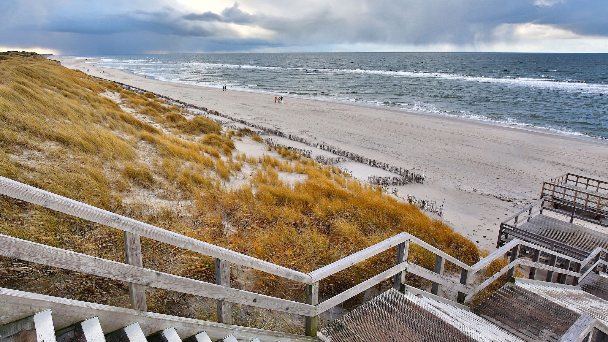 Eine Holztreppe führt über eine Düne bis zum Strand entlang. Von der Treppe aus kann weit auf das Meer gucken.