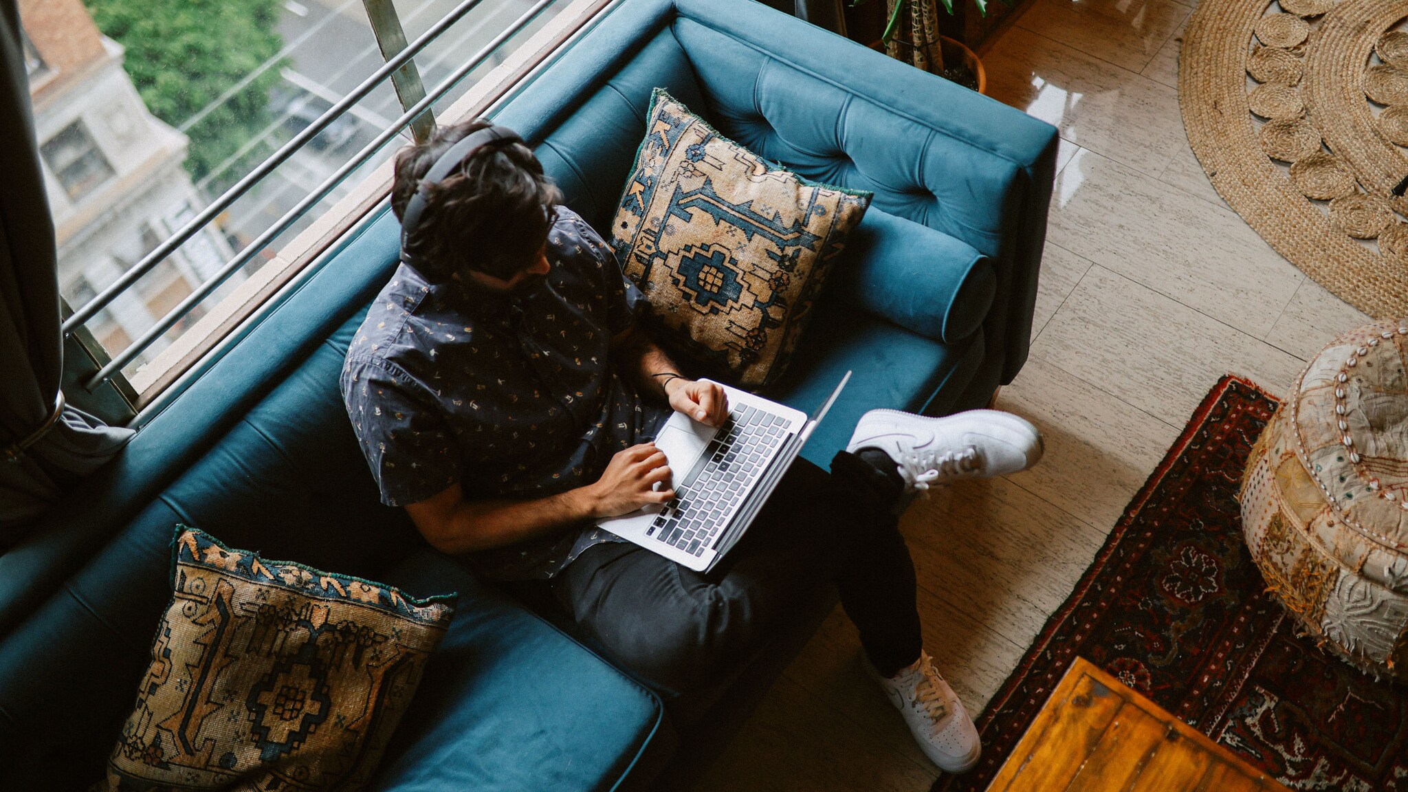 Draufsicht eines Mannes, der auf einem Sofa sitzt und einen aufgeklappten Laptop auf dem Schoß hat.