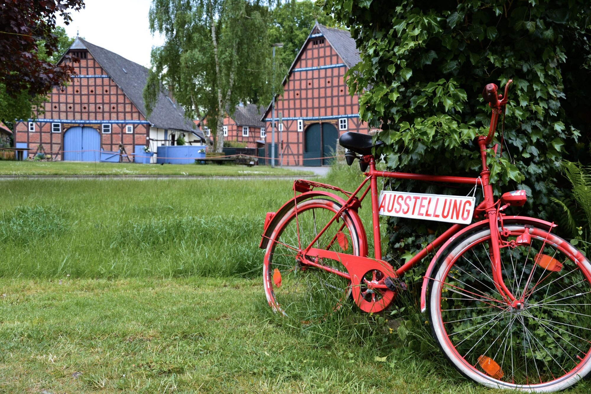 Ein an einen Baum gelehntes, rotes Fahrrad weist zu einer Ausstellung im Wendland