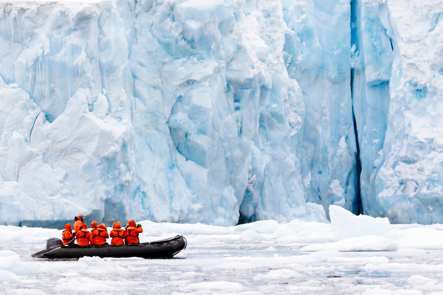 Ein Schlauchboot mit mehreren Personen vor einer gigantischen Eiswand Ein Schlauchboot mit mehreren Personen vor einer gigantischen Eiswand