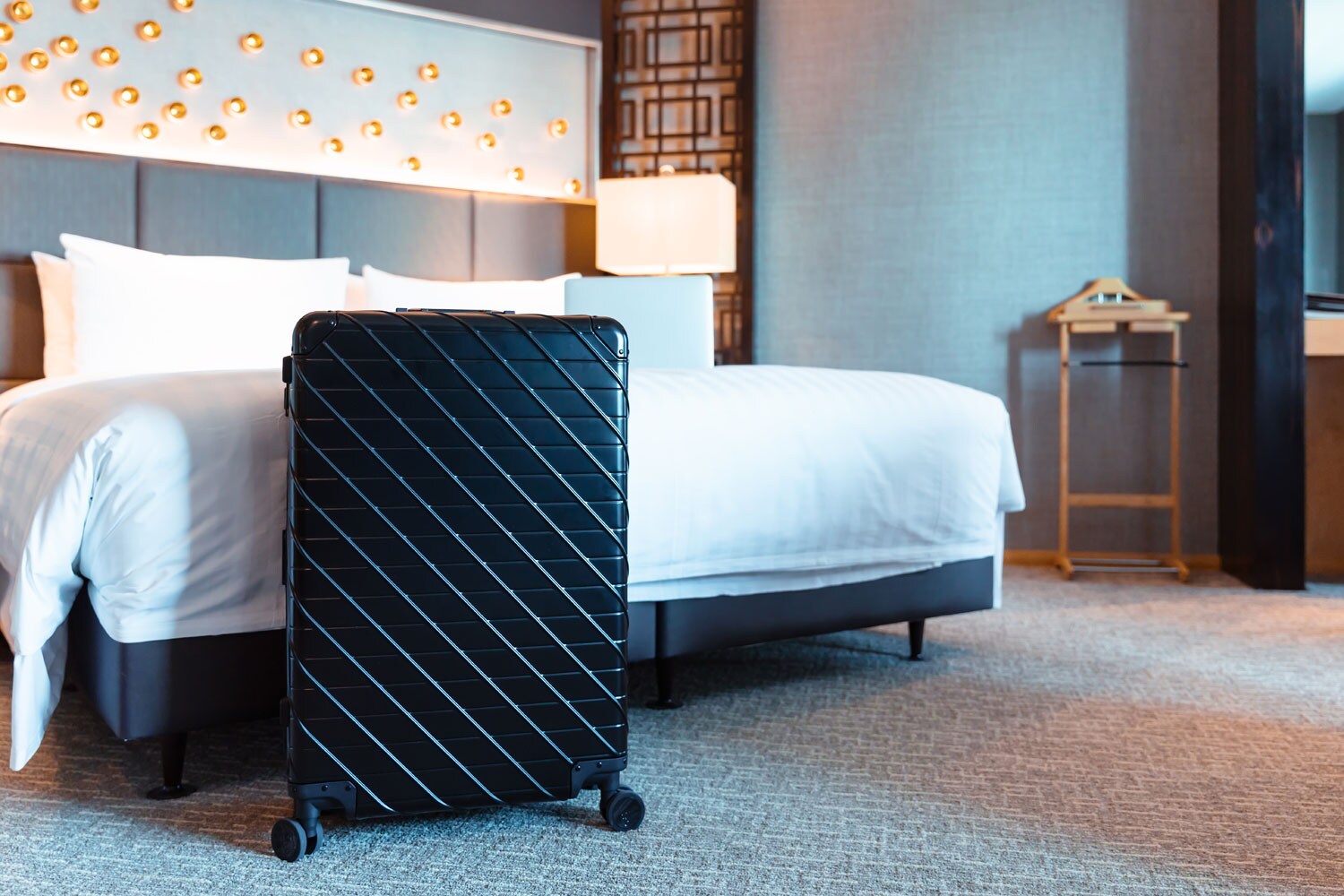 Ein schwarzer Koffer steht in einem Hotelzimmer vor dem Bett Ein schwarzer Koffer steht in einem Hotelzimmer vor dem Bett