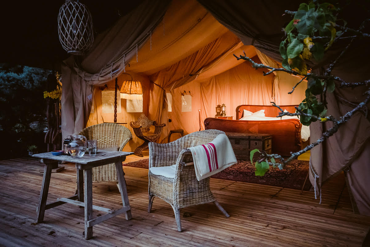 Glamping-Zelt mit Holzbett sowie Tisch und Stühlen Glamping-Zelt bei Nacht