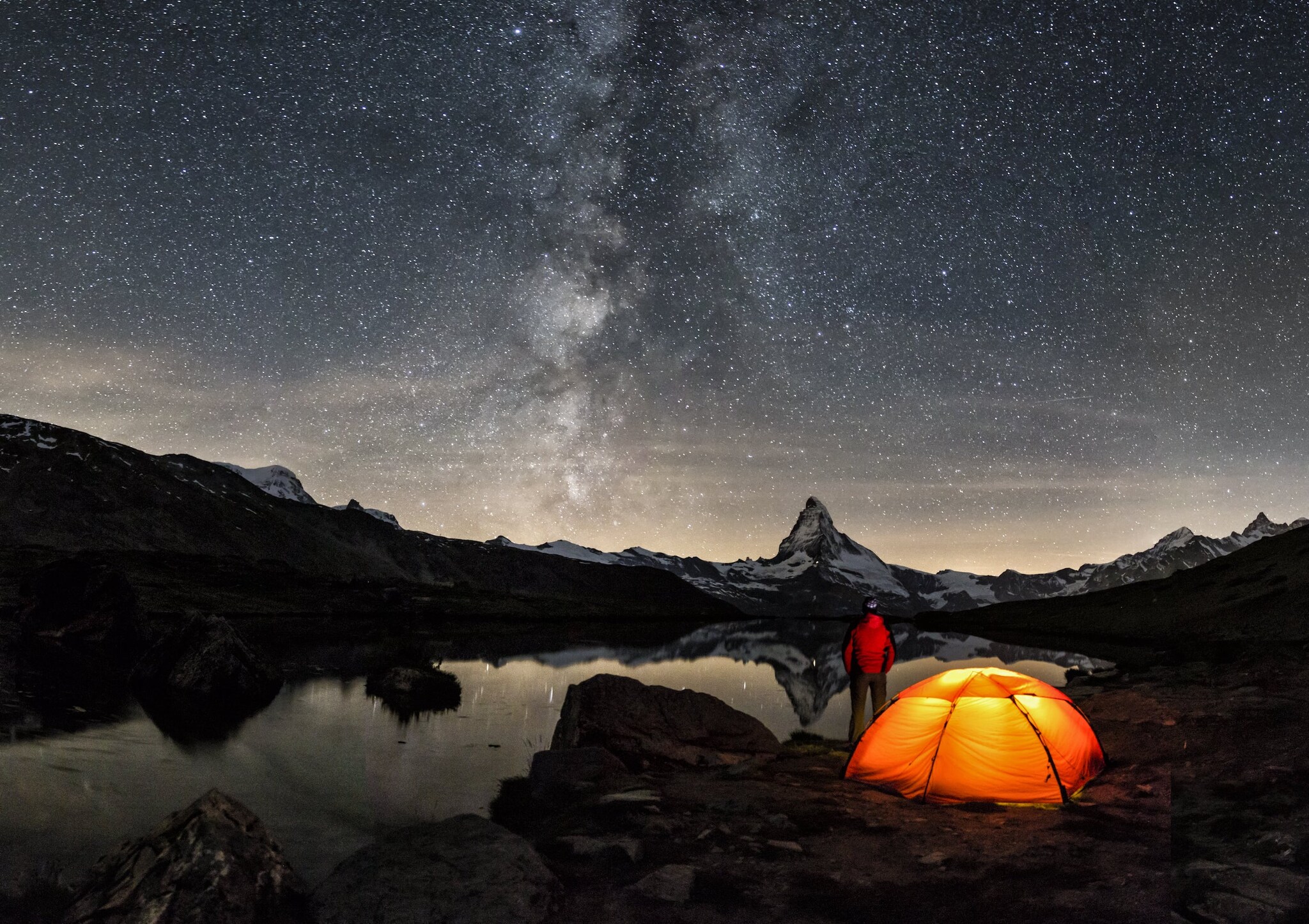 Sternenhimmel über dem Matterhorn, im Vordergrund leuchtet in der kargen Landschaft ein beleuchtetes Zelt Sternenhimmel über dem Matterhorn, im Vordergrund leuchtet in der kargen Landschaft ein beleuchtetes Zelt