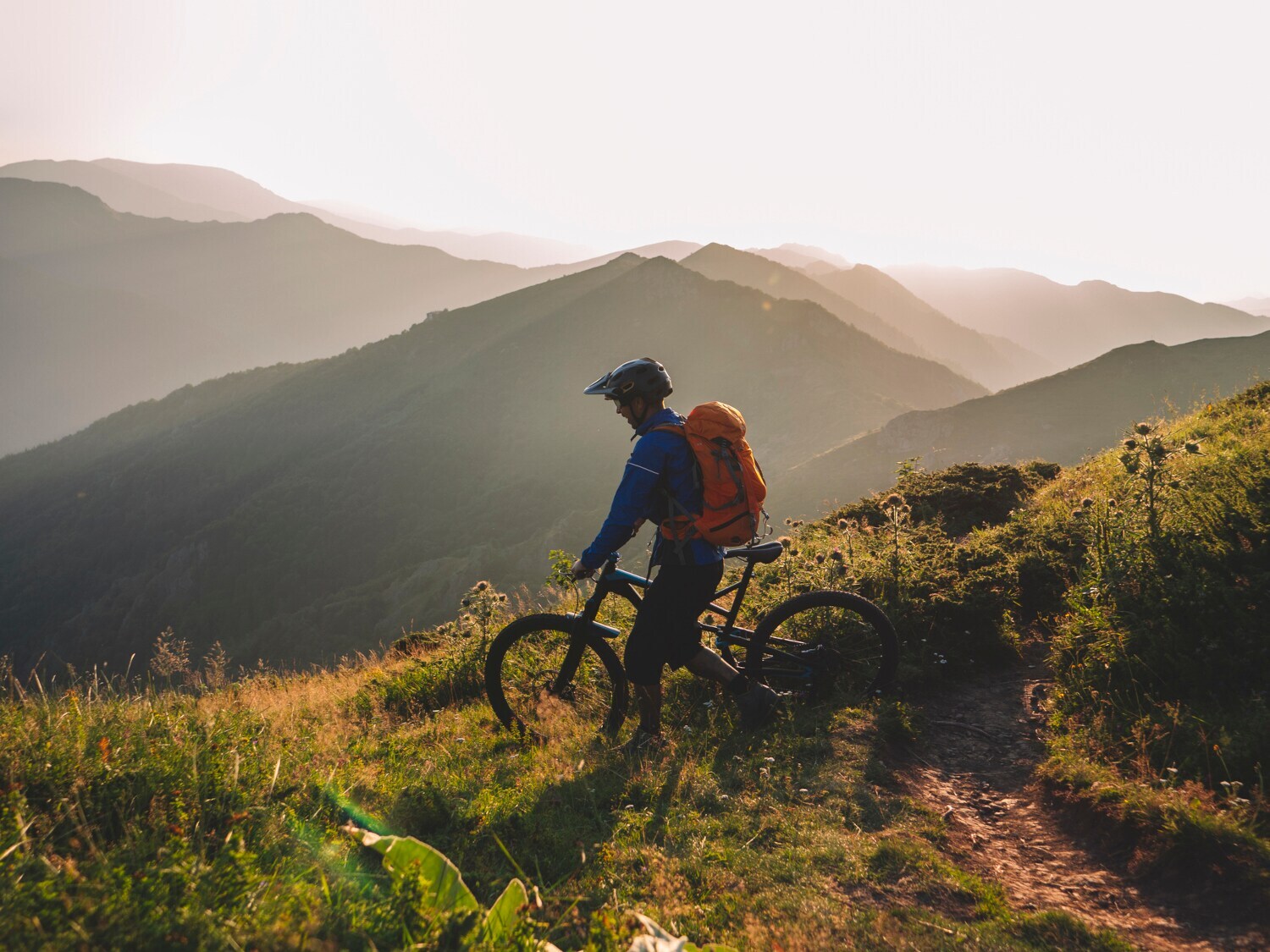 Mountainbiker steht mit seinem Rad auf einem Berg und schaut ins Tal
