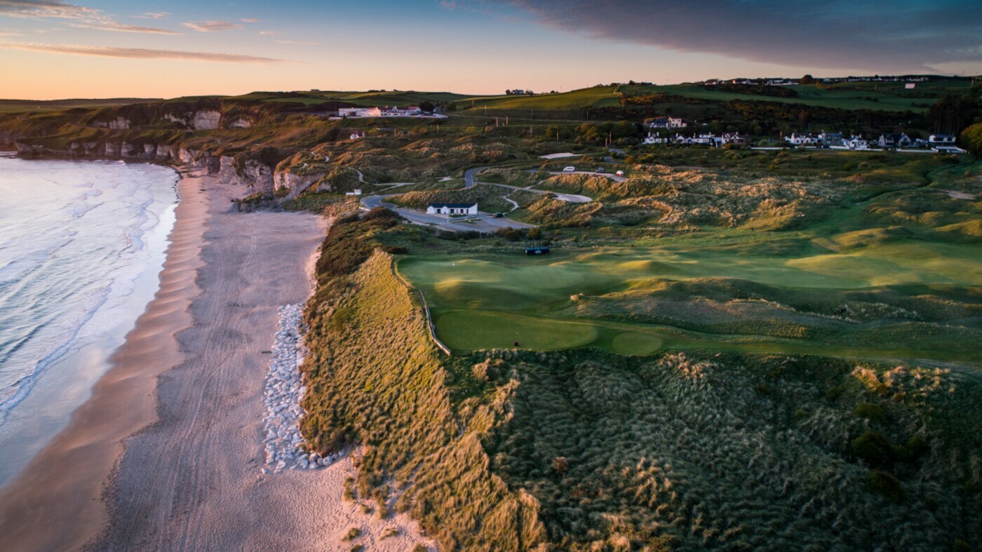 Blick auf einen Golfplatz und einen Küstenstreifen mit Sandstrand aus der Luft