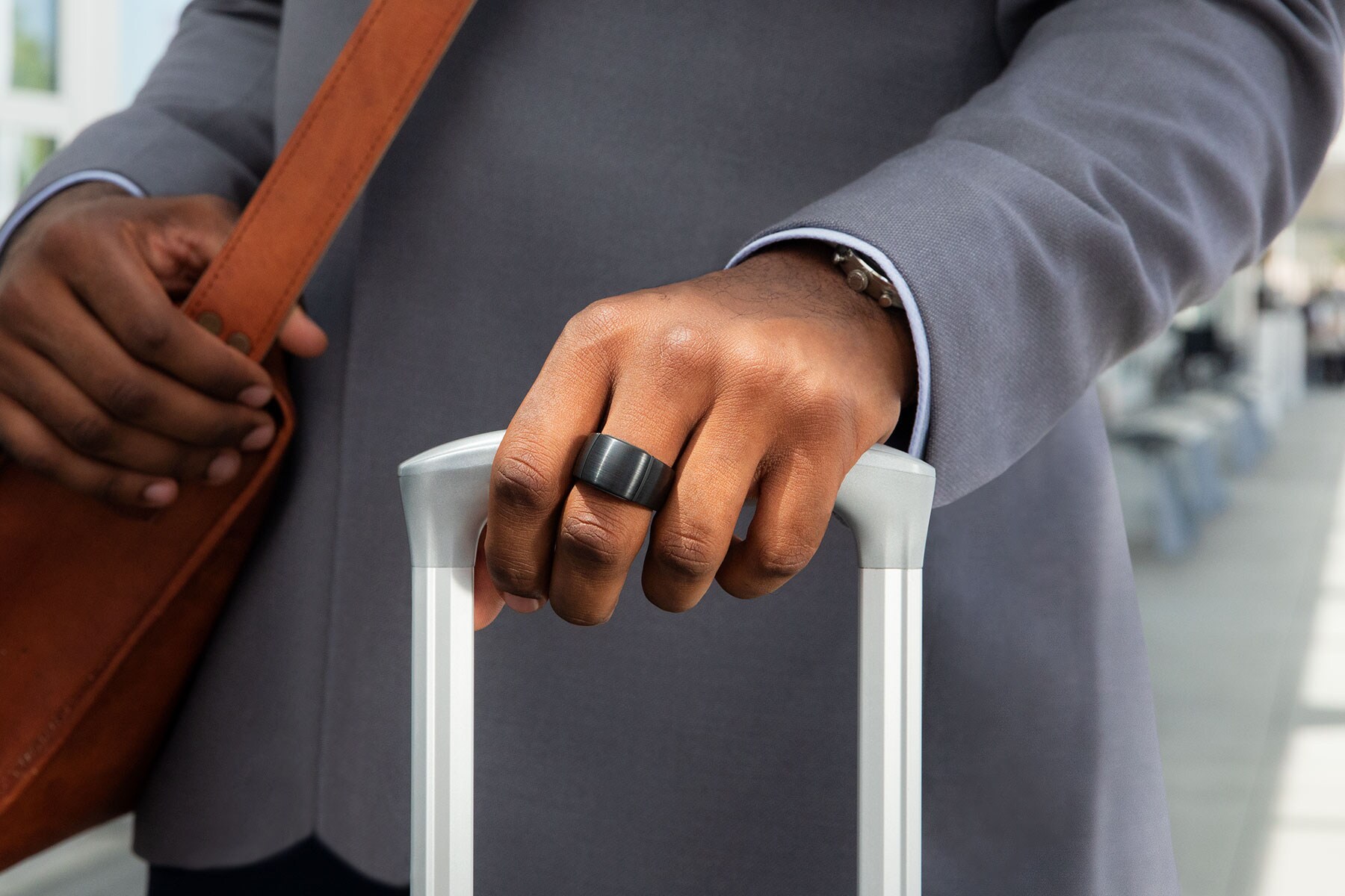 Ein Smart Ring am Mittelfinger einer Hand, die einen Trolley hält