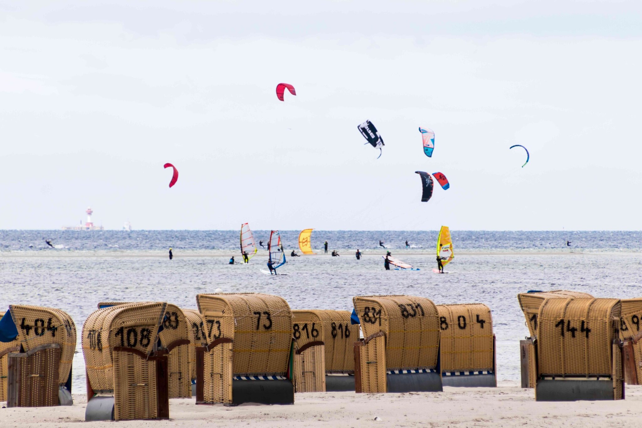 Strandkörbe an Land und Surfer:innen im Wasser in der Ostsee