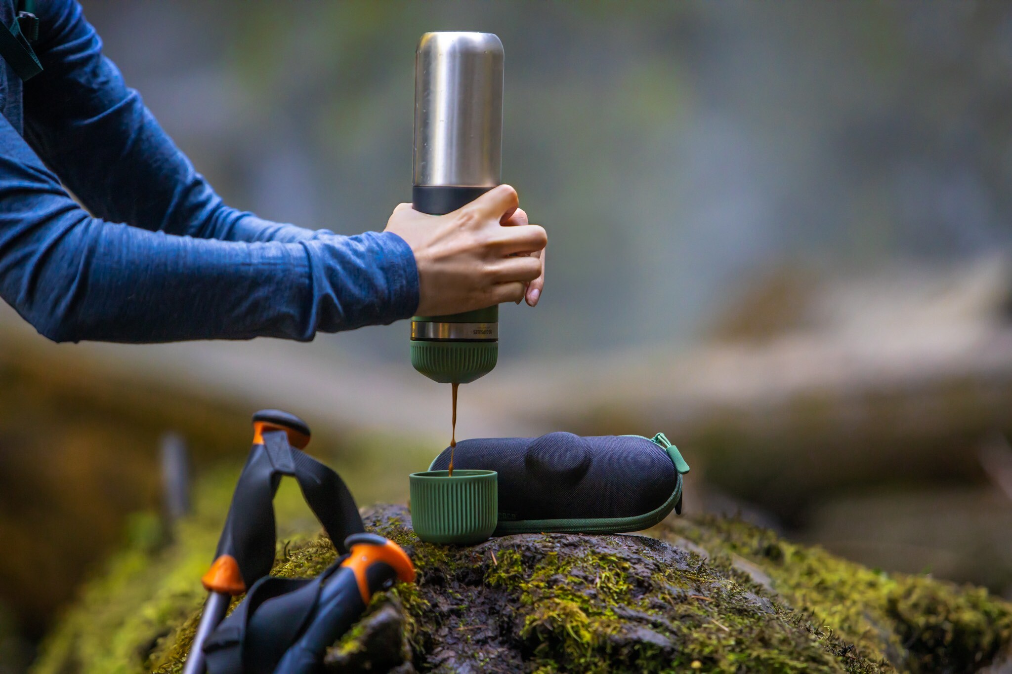 Eine Frau gießt sich bei einer Wanderung einen Espresso aus einer Thermoskanne in einen Becher.