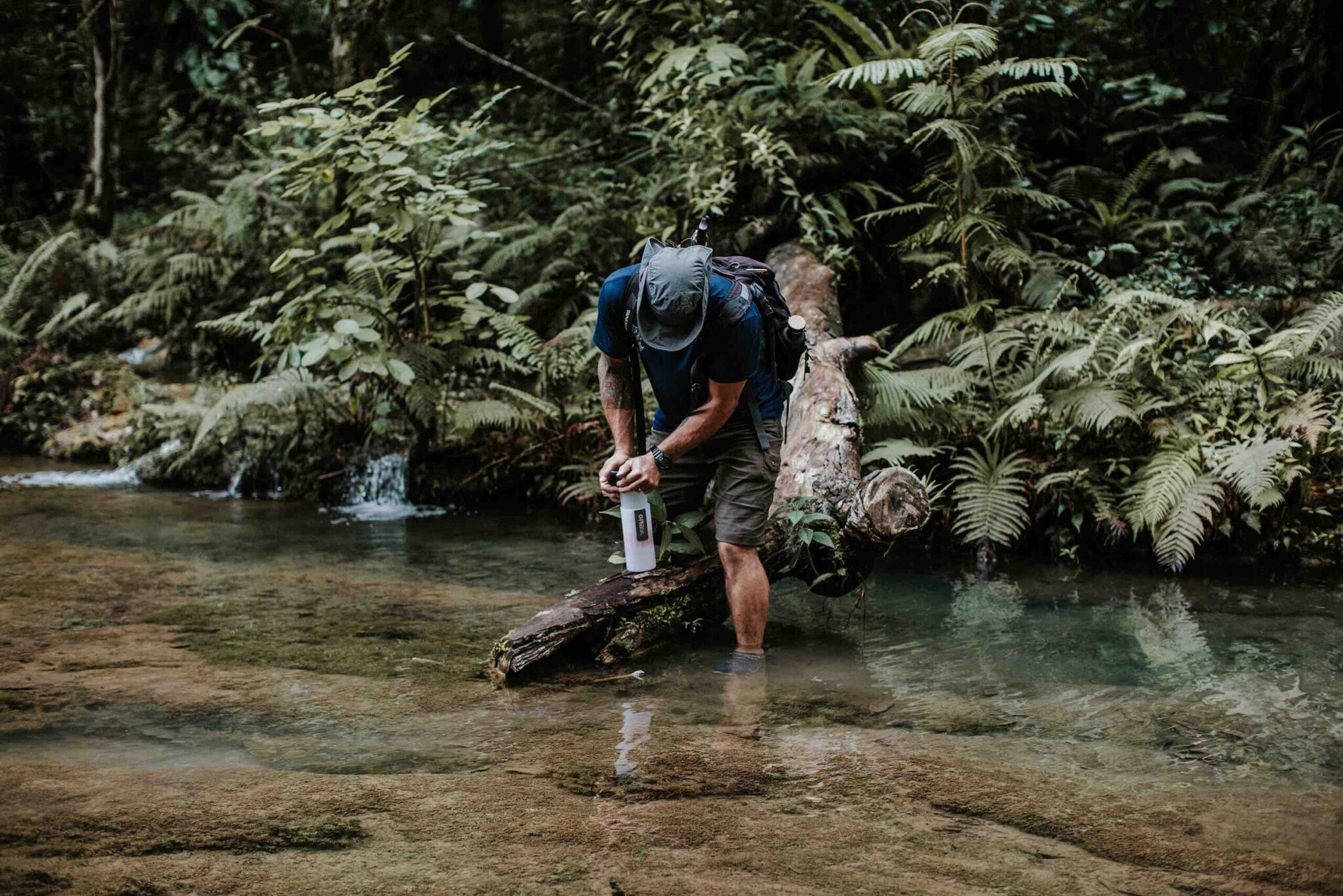 Ein Mann in Shorts steht in einem klaren Fluss und und füllt Wasser in eine Trinkflasche. Ein Mann in Shorts steht in einem klaren Fluss und und füllt Wasser in eine Trinkflasche.