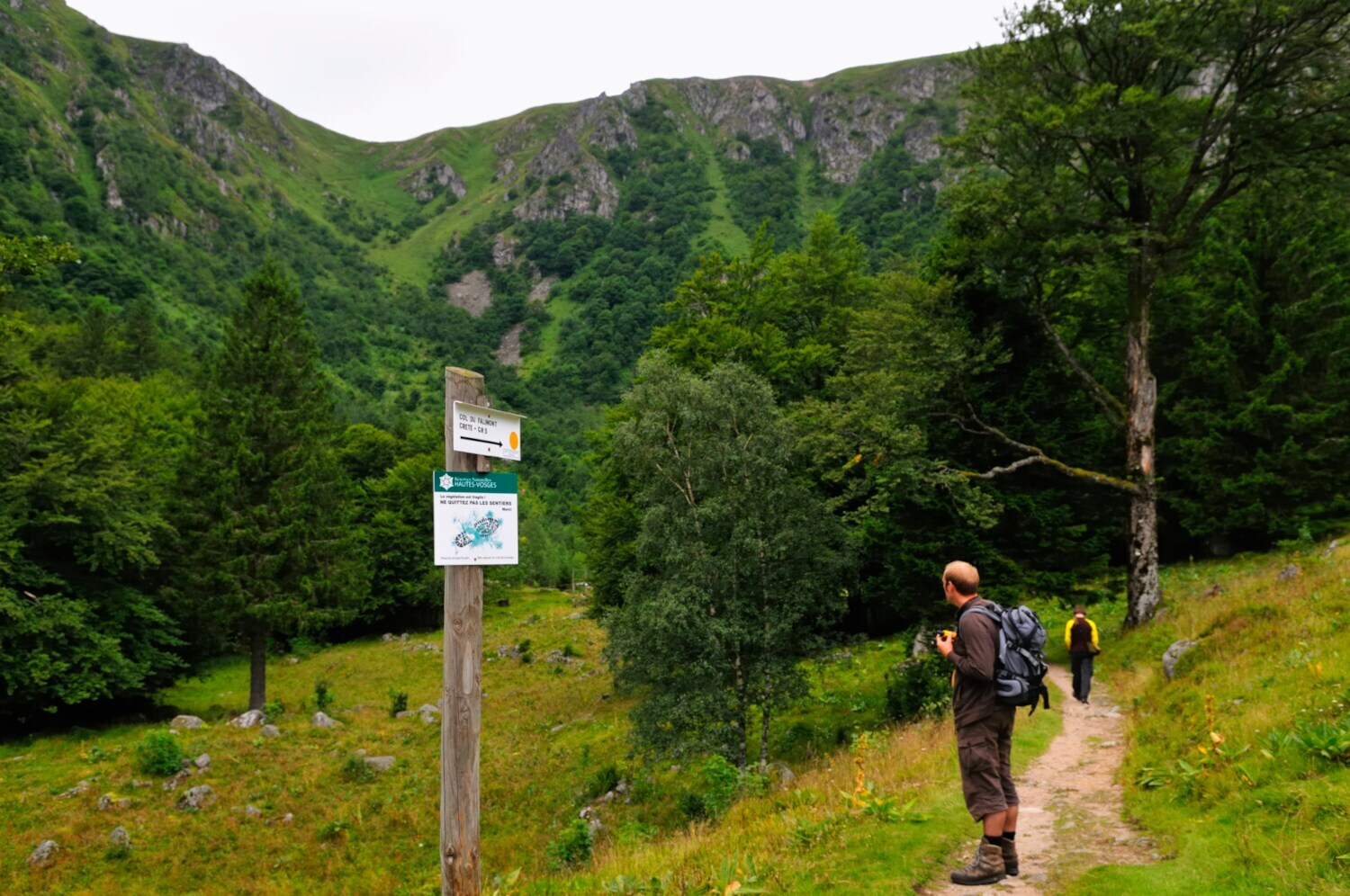 Ein Mann steht vor einem Wegweiser im Hintergrund sind Bäume und Felsen