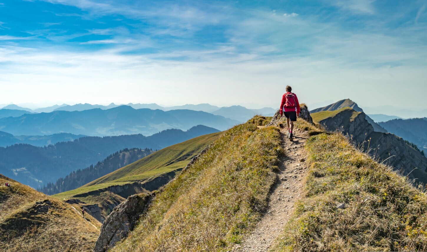 Rückansicht einer Person mit rotem Rucksack auf einem Wanderweg in den Bergen