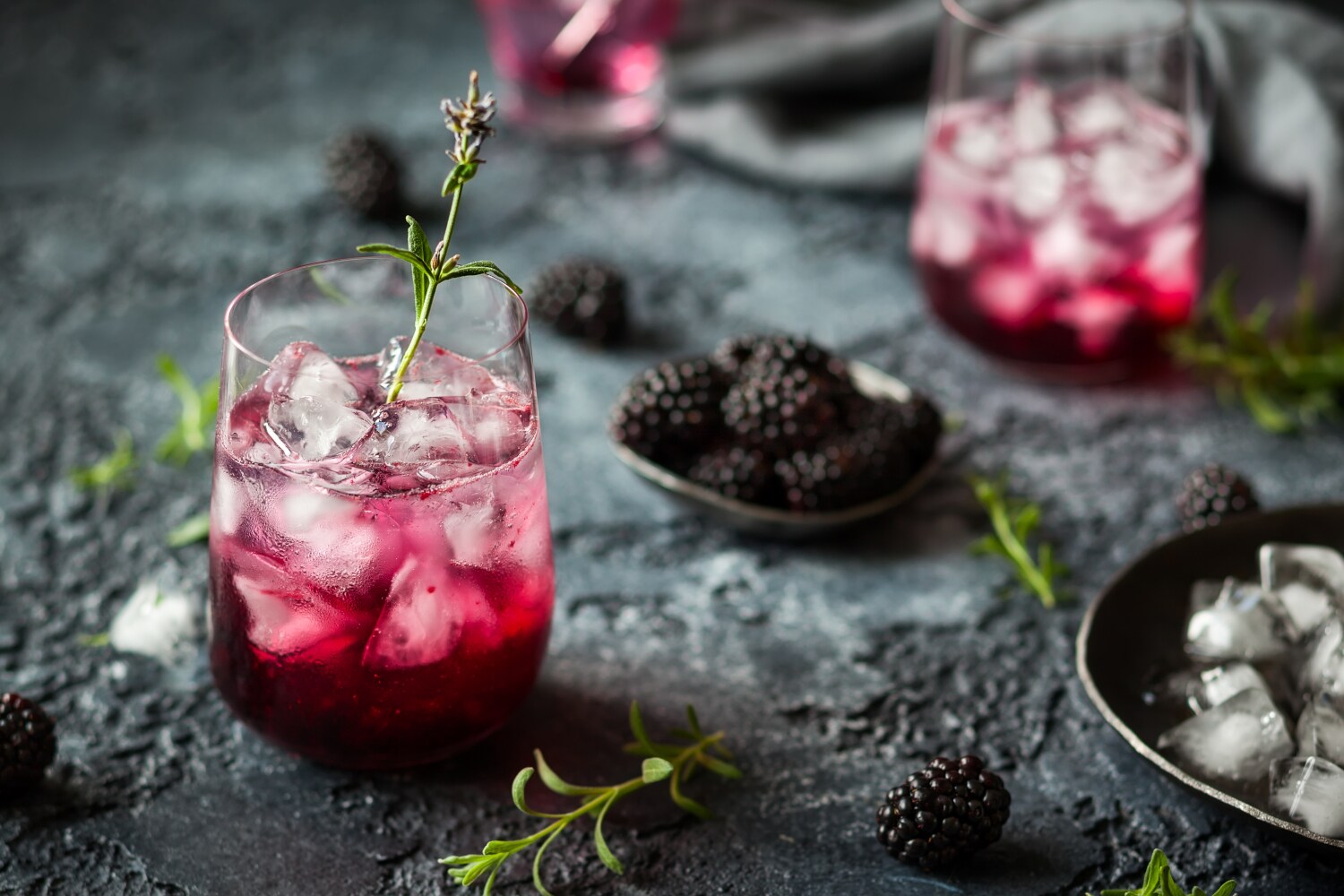 Ein Glas mit einem rötlich gefärbten Longdrink, Kräutern und Brombeeren