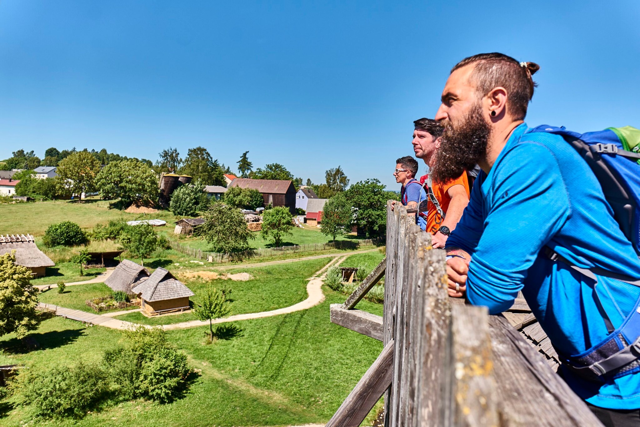 Wandernde stehen an einem Holzzaun von dem aus sie auf den Geschichtspark blicken