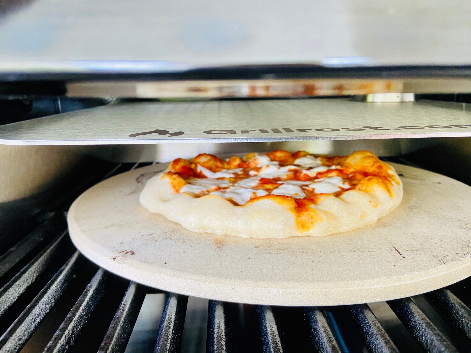 Pizza auf einem runden Stein der auf einem Rost liegt und ein Metallaufsatz darüber
