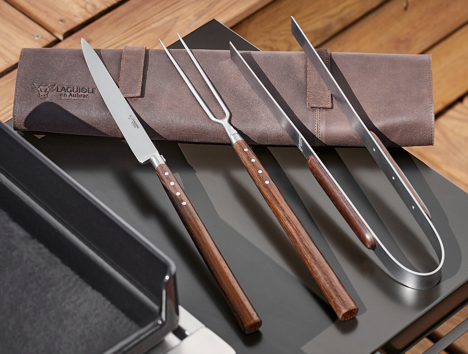 Ein Grillset liegt auf einer Ledertasche auf einem Tisch