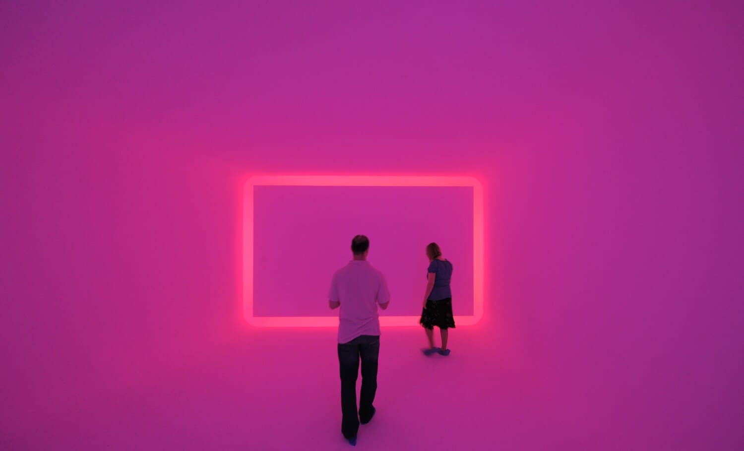 Zwei Museumsbesucher:innen in einem Raum, der pink beleuchtet ist Zwei Museumsbesucher:innen in einem Raum, der pink beleuchtet ist