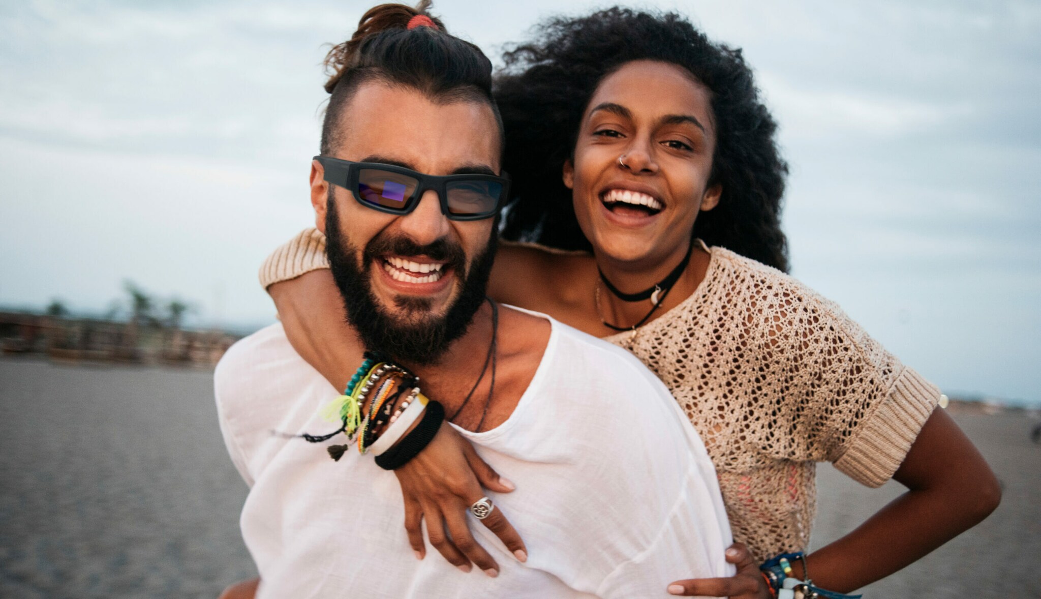 Ein Paar lachend am Strand, er trägt eine Sonnenbrille Ein Paar lachend am Strand, er trägt eine Sonnenbrille