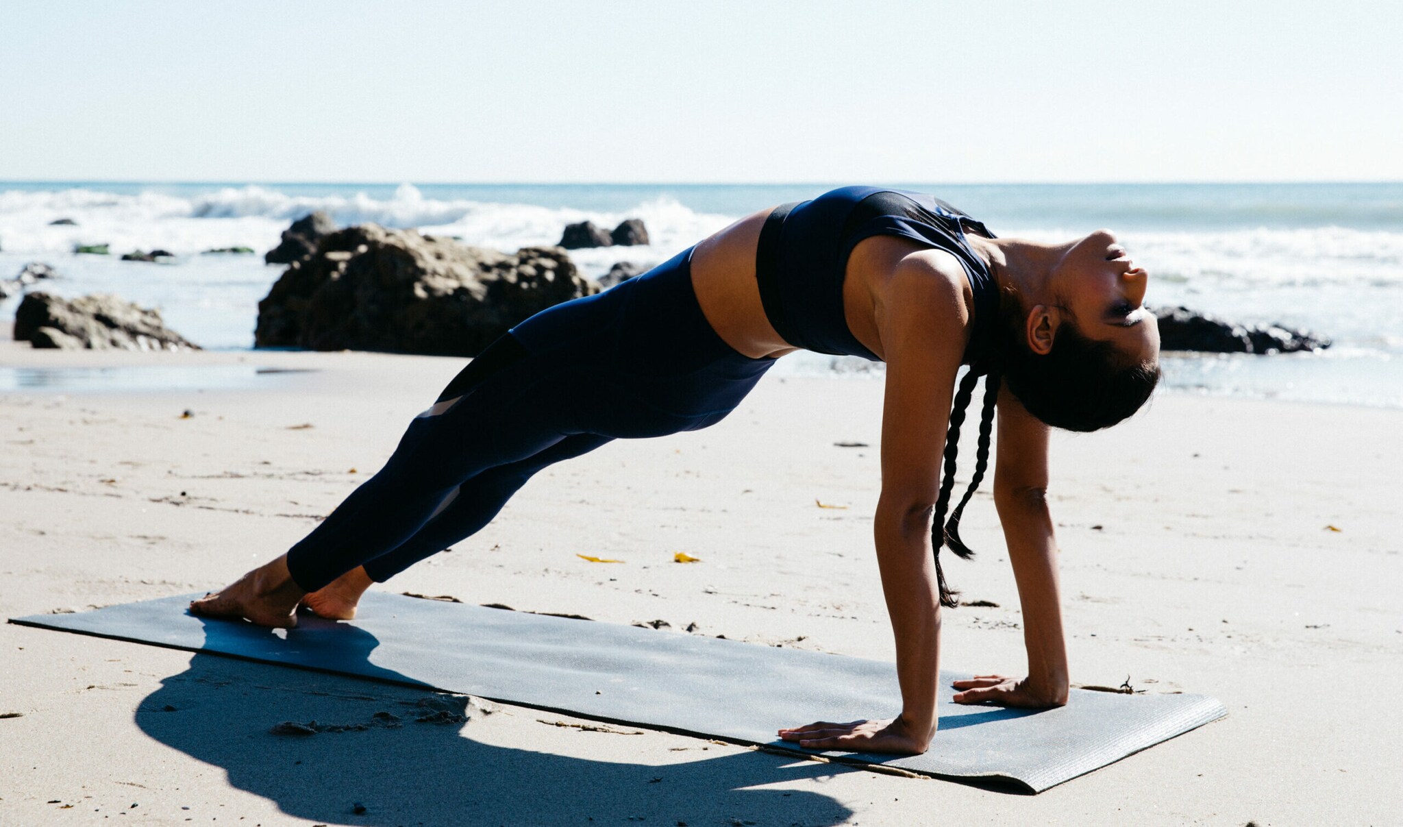 Eine Frau auf einer Matte am Strand in einer Yogaposition