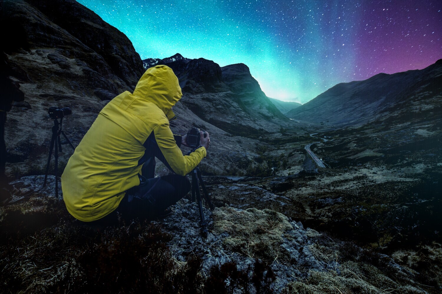 Eine Person in wasser- und windabweisender Kleidung fotografiert einen lila-blau leuchteten Sternenhimmel