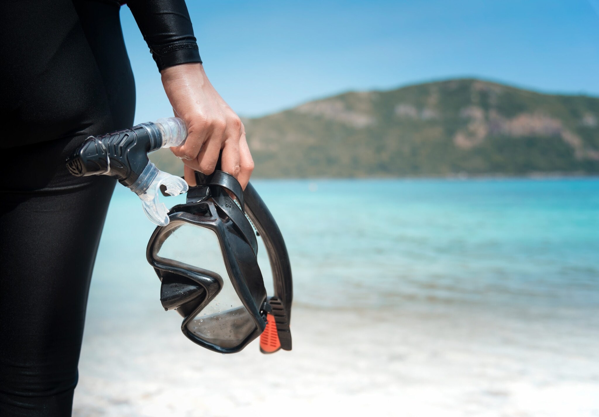 Eine Person am Strand hält eine Taucherbrille und einen Schnorchel Eine Person am Strand hält eine Taucherbrille und einen Schnorchel