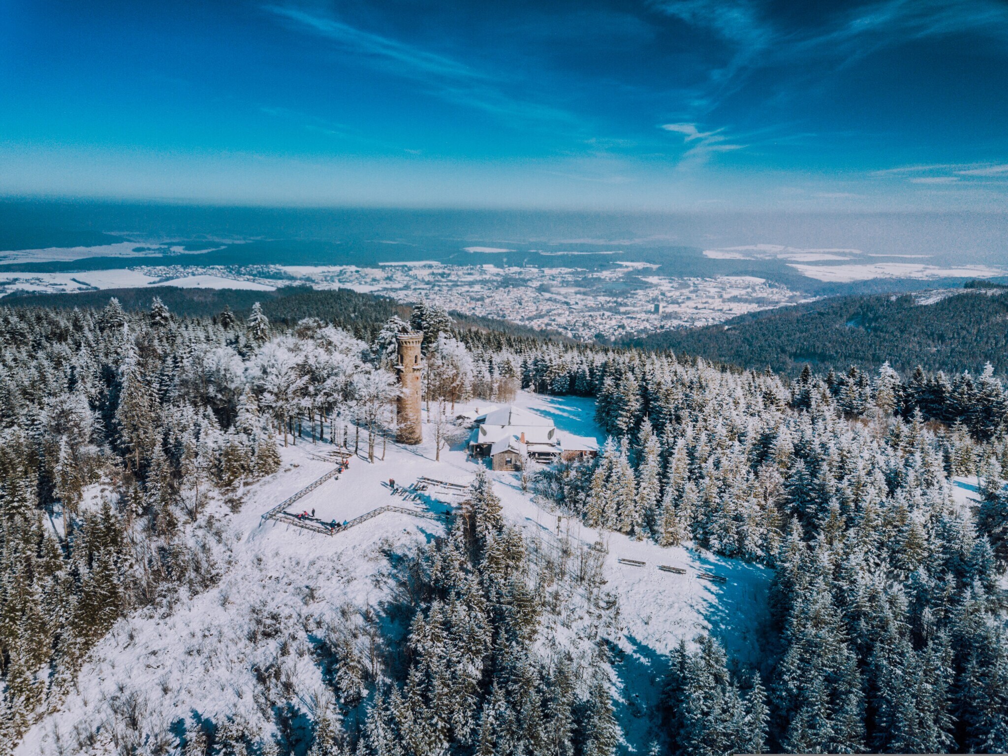 Luftaufnahme eines verschneiten Berges in einem Mittelgebirge mit einem Turm auf dem Gipfel