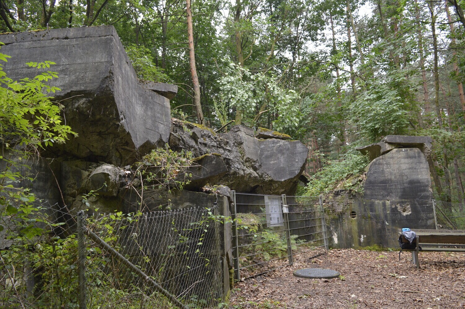 Hinter einem Zaun liegen massive und marode Steinplatten aufeinander