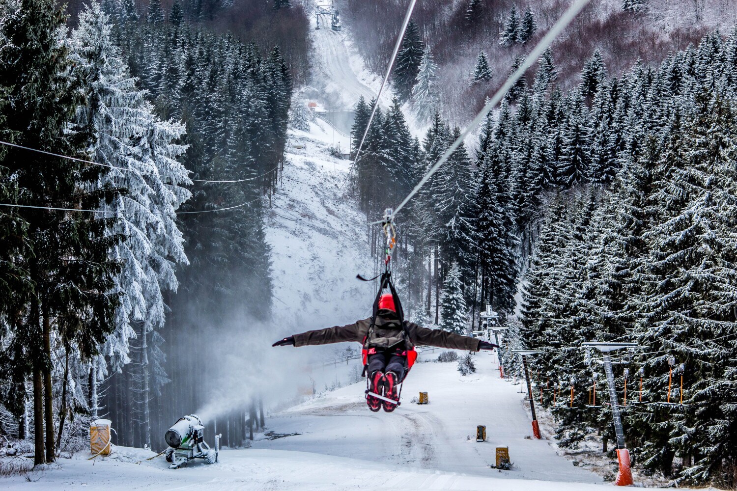 Eine Person in Winterkleidung überquert an der Zipline ein schneebedecktes Waldgebiet