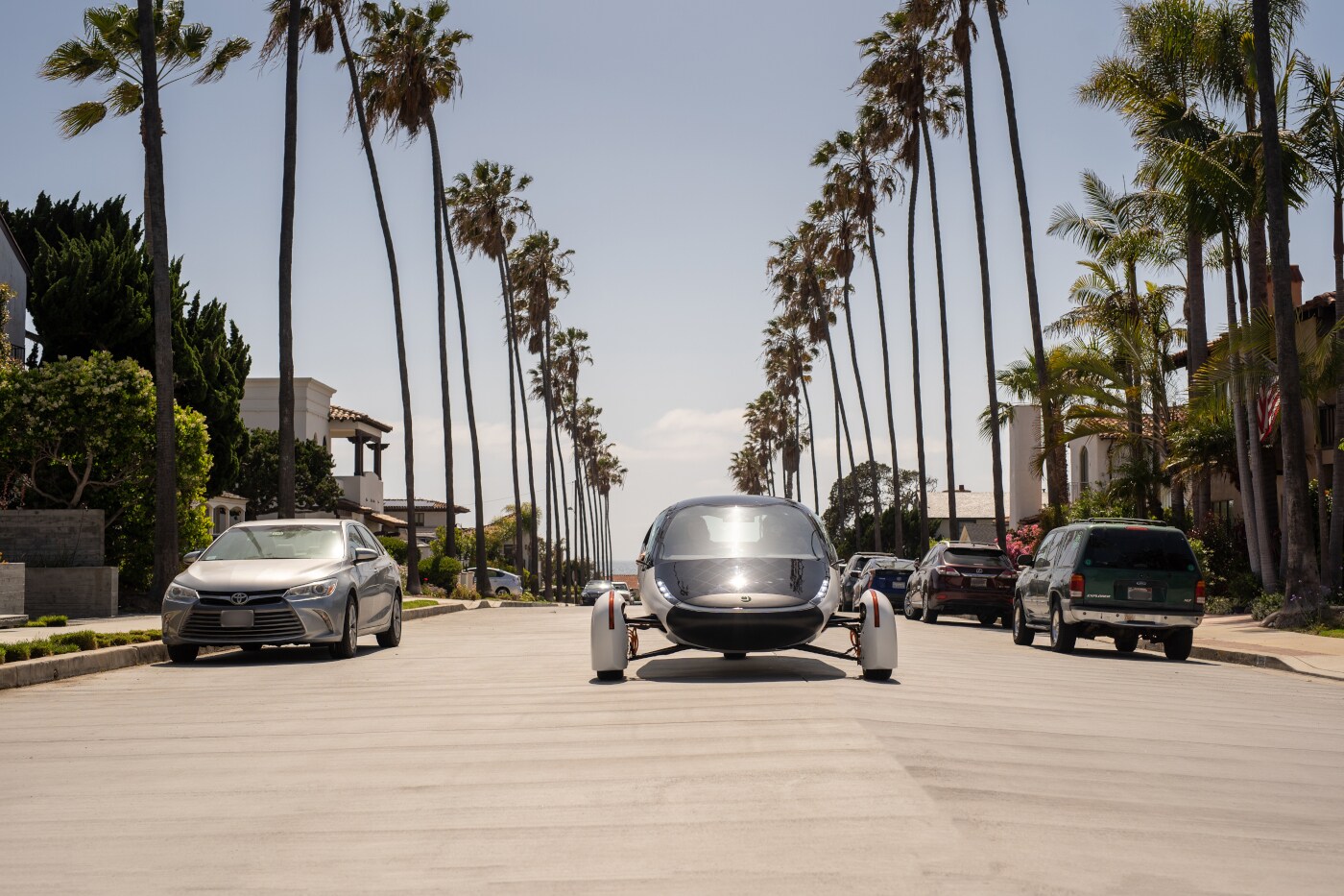 Ein futuristisches Fahrzeug fährt in der Sonne auf palmengesäumter Straße