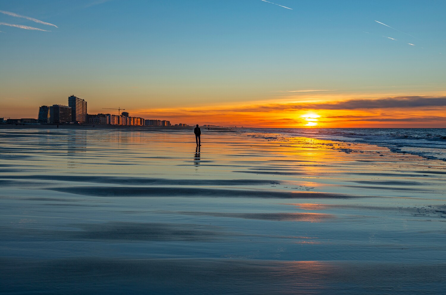 Eine Person am Strand bei Sonnenuntergang vor einer Stadt im Hintergrund Eine Person am Strand bei Sonnenuntergang vor einer Stadt im Hintergrund