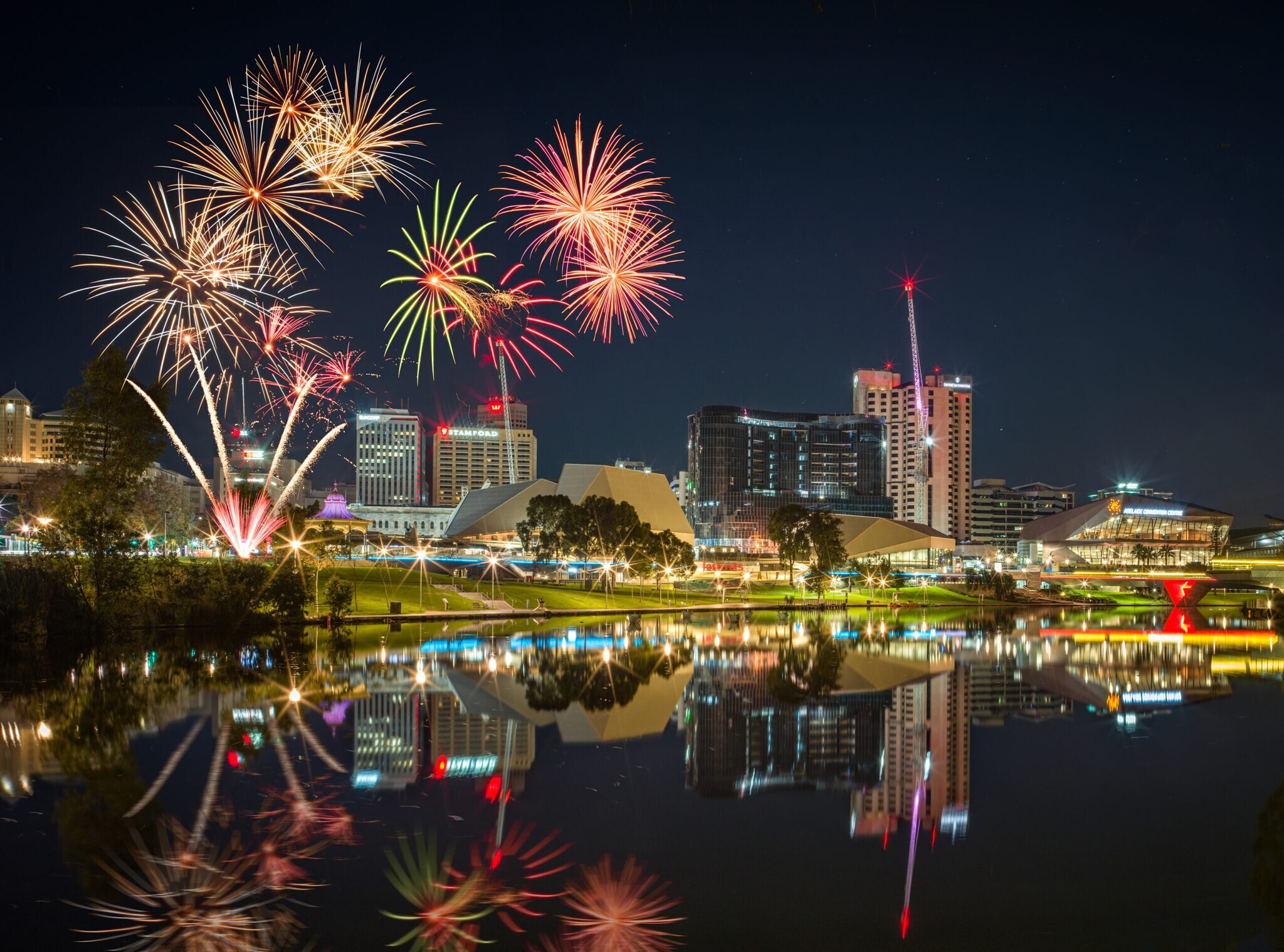 In einer Wasserfläche spiegeln sich das dahinterliegende Feuerwerk und Gebäude In einer Wasserfläche spiegeln sich das dahinterliegende Feuerwerk und Gebäude