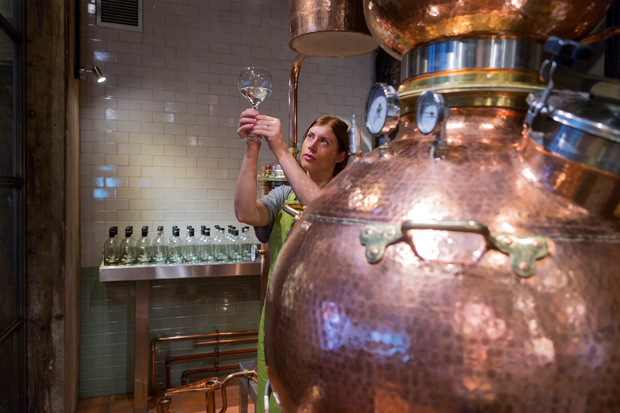 Eine Frau steht neben einem Brennerei-Kessel aus Kupfer