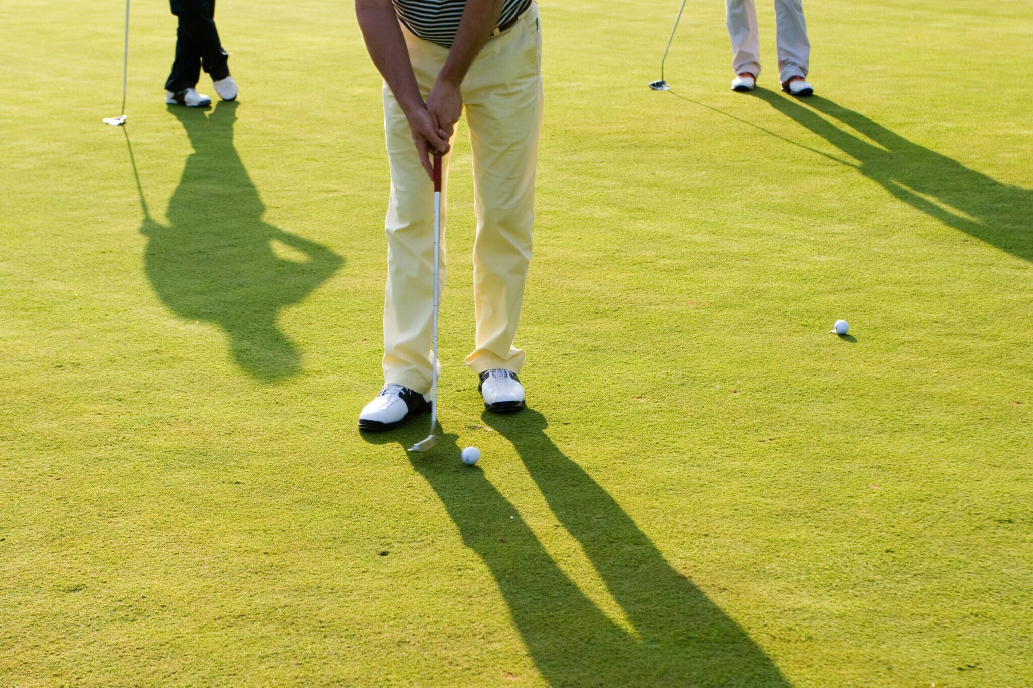 Drei Beinpaare mit Golfschlägern und -bällen auf Rasen