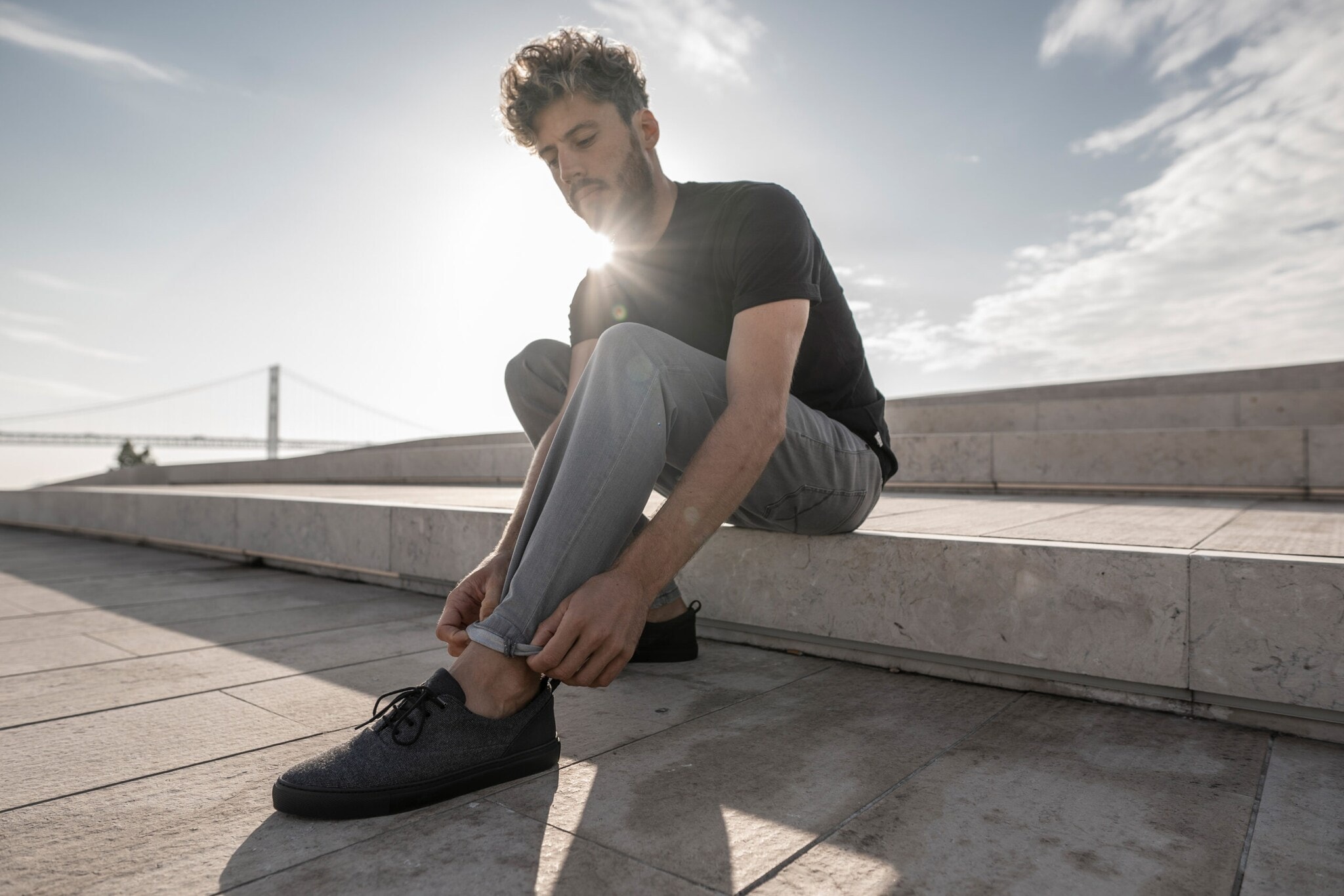 Ein Mann sitzt auf einer Holzpromenade auf einer Steinstufe, die Füße mit schwarzen Sneakern im Vordergrund Ein Mann sitzt auf einer Holzpromenade auf einer Steinstufe, die Füße mit schwarzen Sneakern im Vordergrund