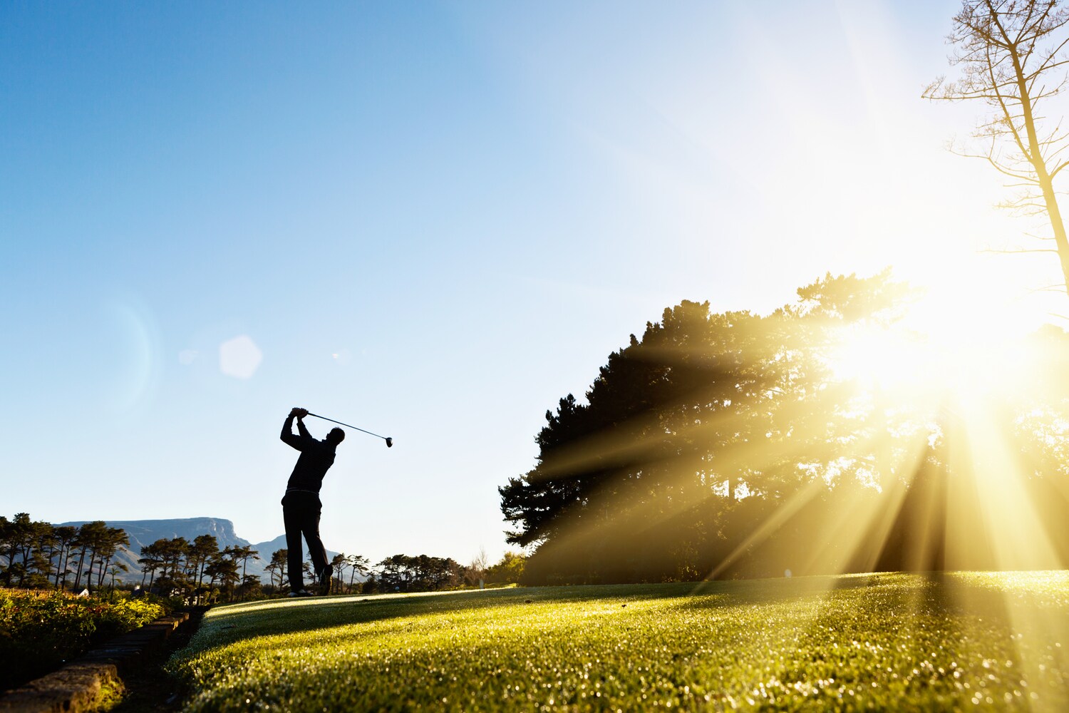 Die Silhouette eines ausholenden Golfspielers im Gegenlicht auf einem Golfplatz