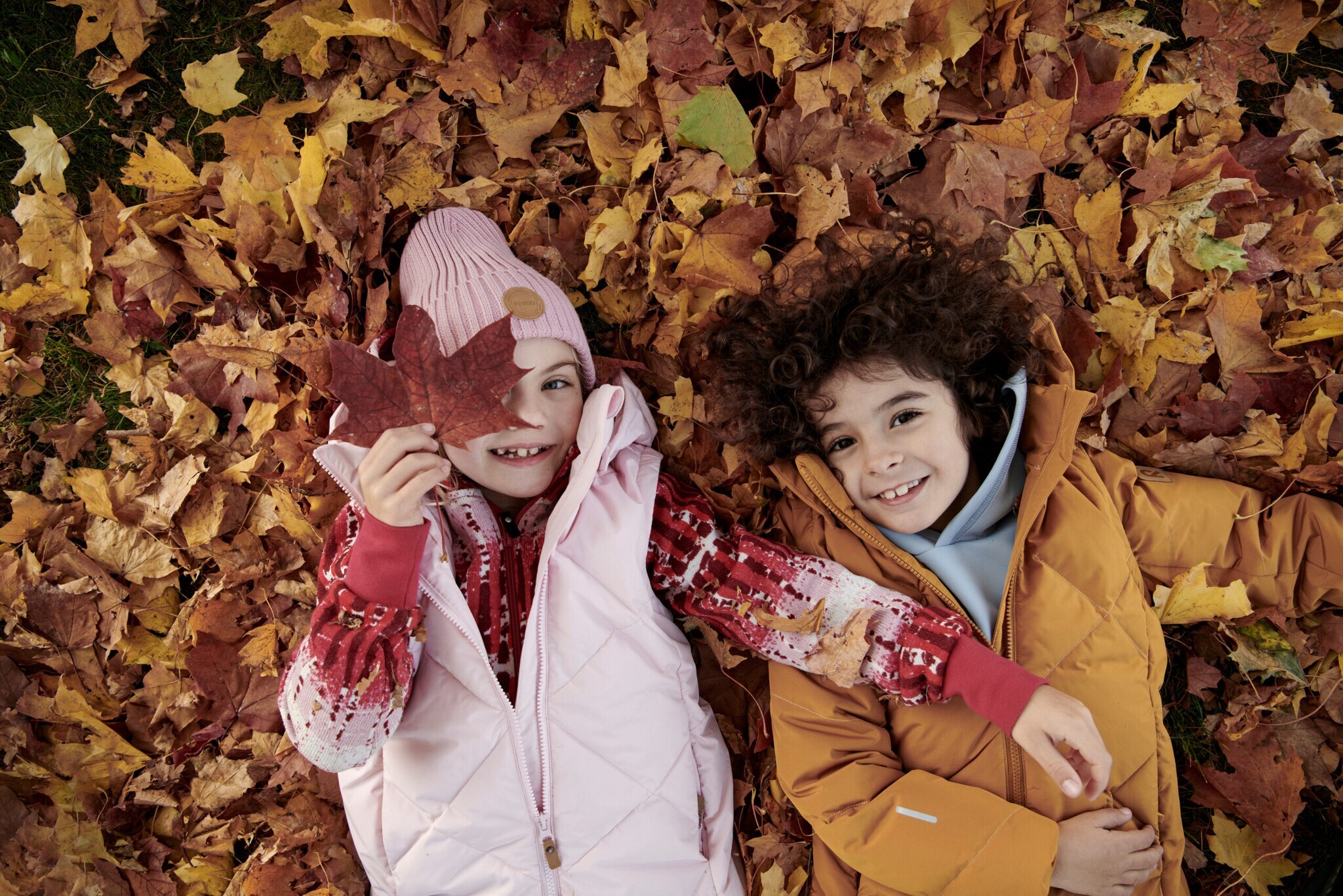 Ein Mädchen und ein Junge liegen lachend im Herbstlaub