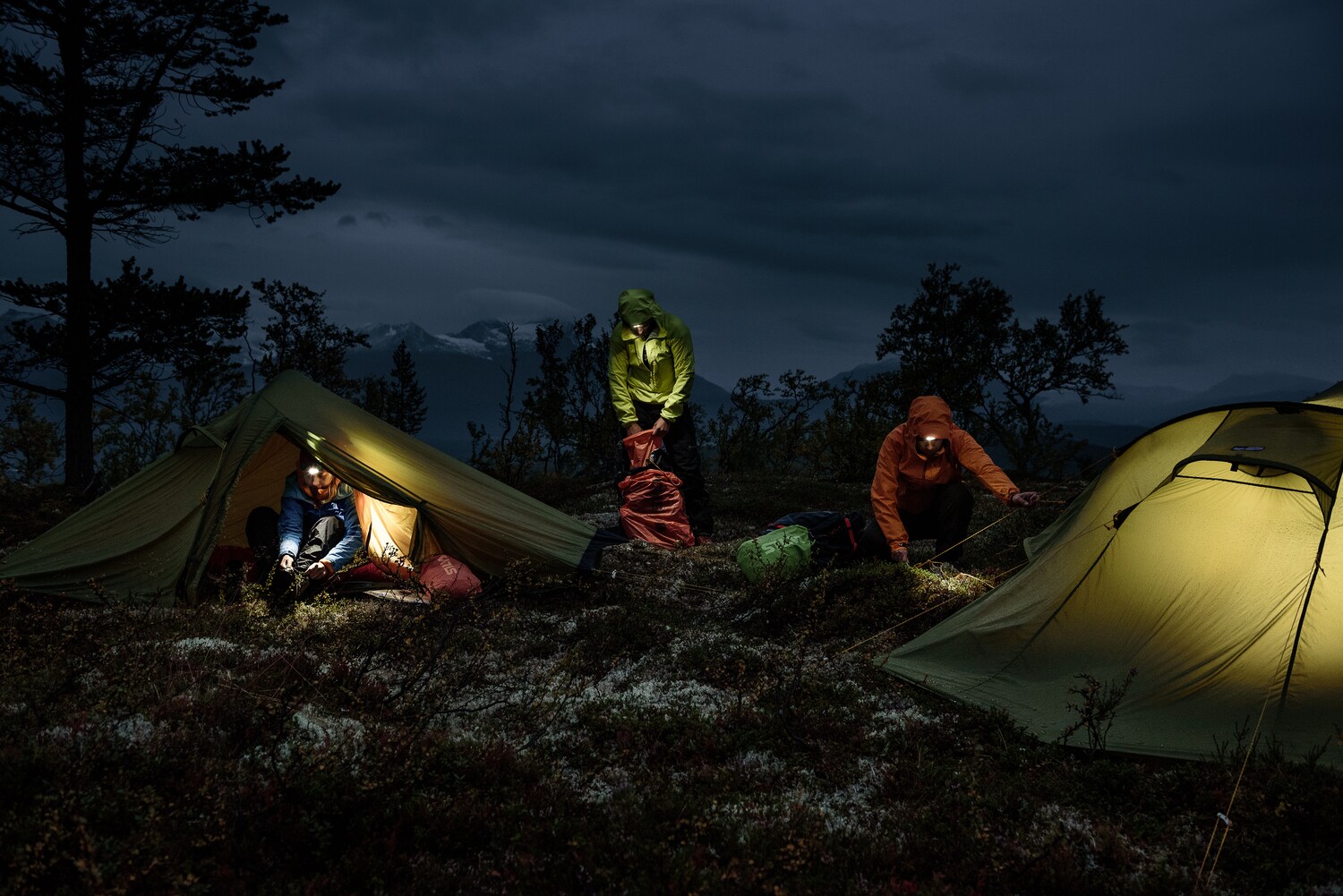 Nachtaufnahme von drei Menschen mit Zelten und Stirnlampen in der Natur Nachtaufnahme von drei Menschen mit Zelten und Stirnlampen in der Natur