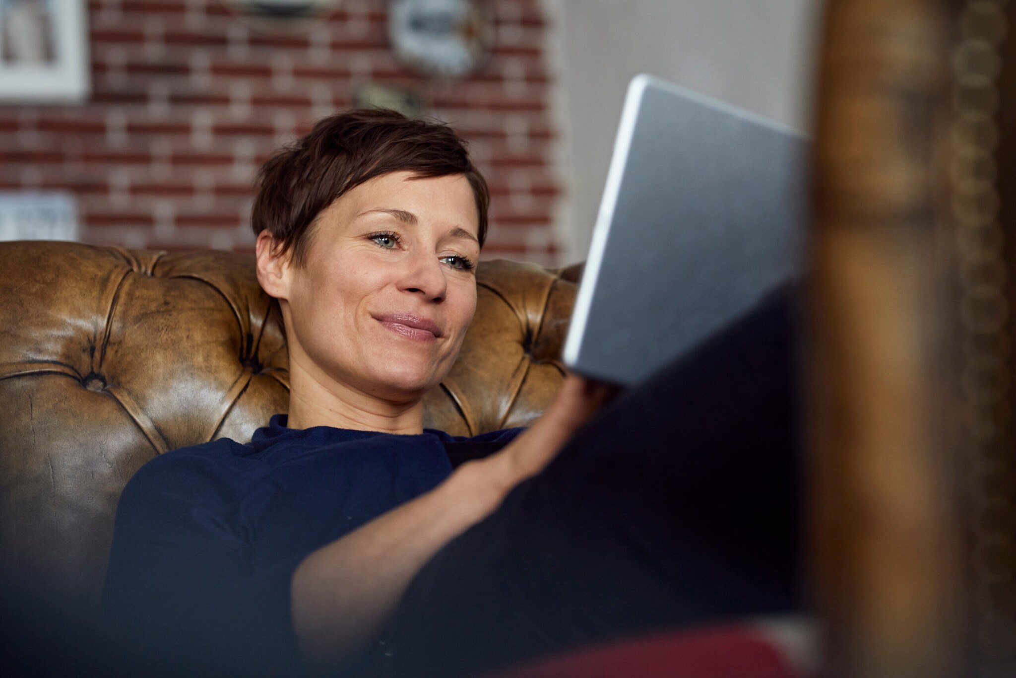 Eine Frau auf einer Ledercouch schaut zufrieden in ihr Tablet