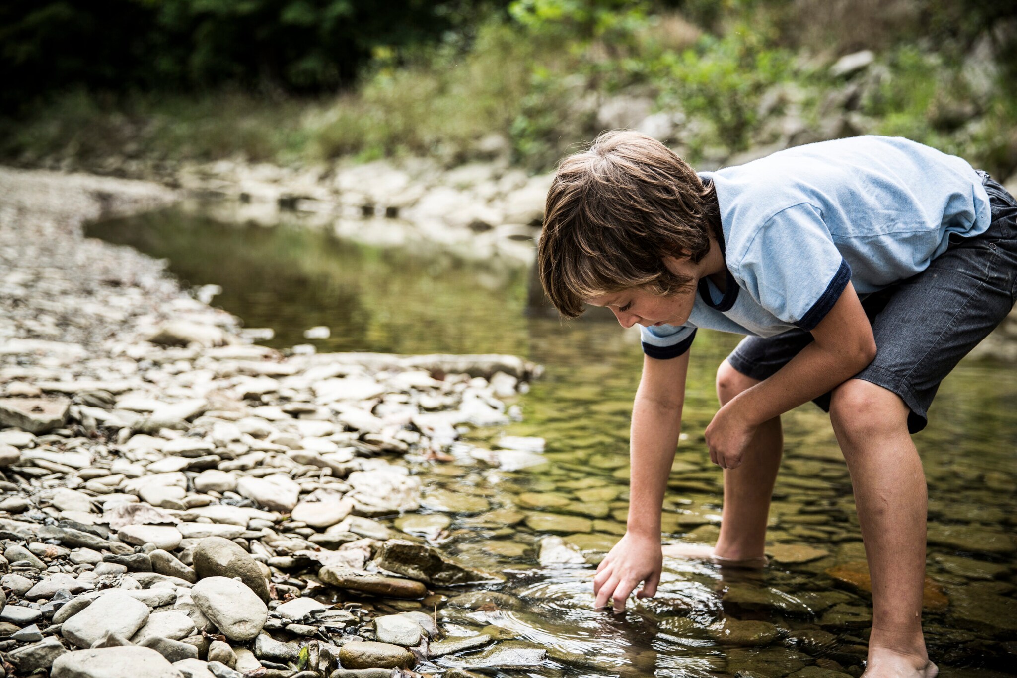 Ein Junge steht in einem Bachlauf und fasst ins Wasser