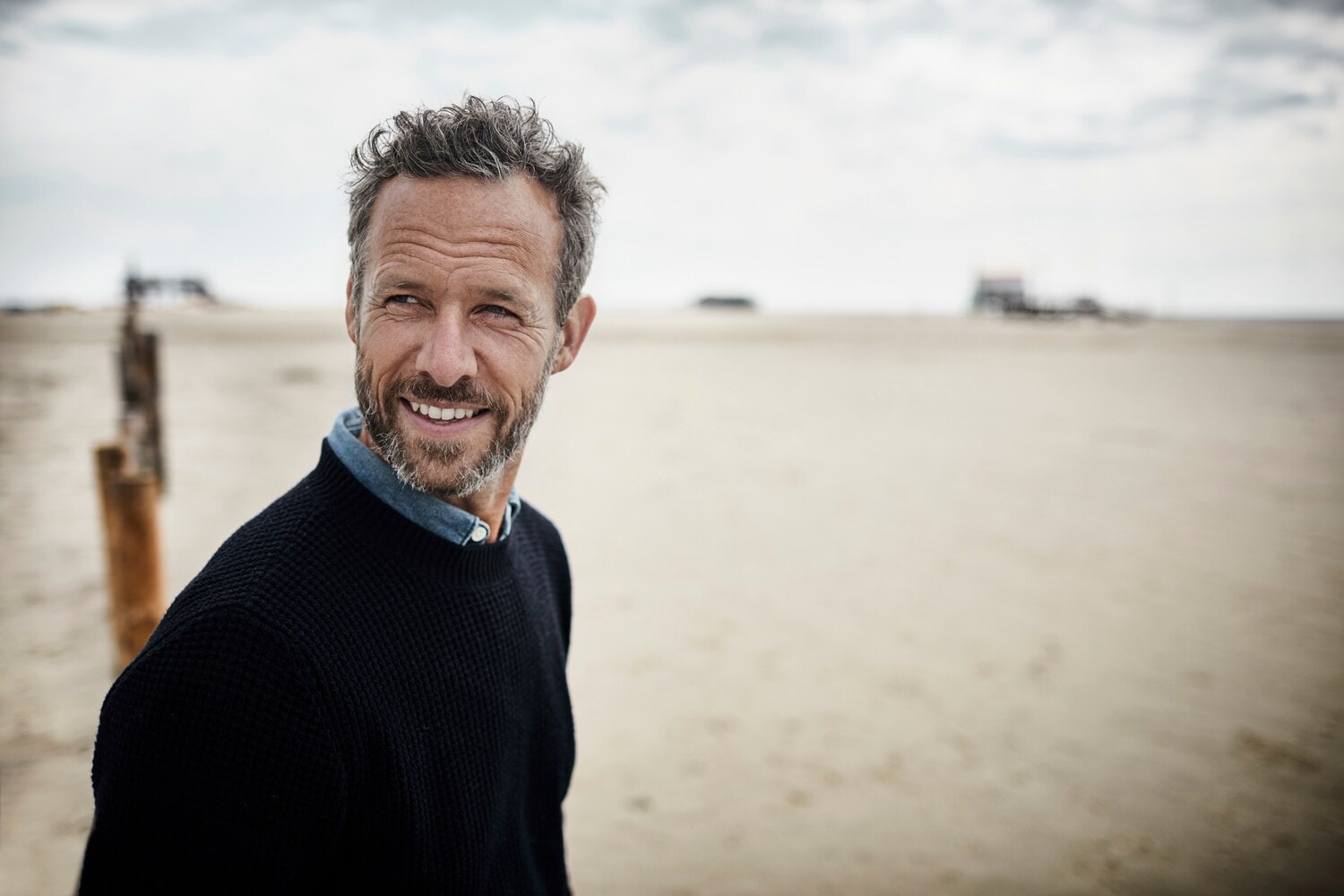 Ein Mann mittleren Alters mit Bart steht am Strand und lächelt Ein Mann mittleren Alters mit Bart steht am Strand und lächelt