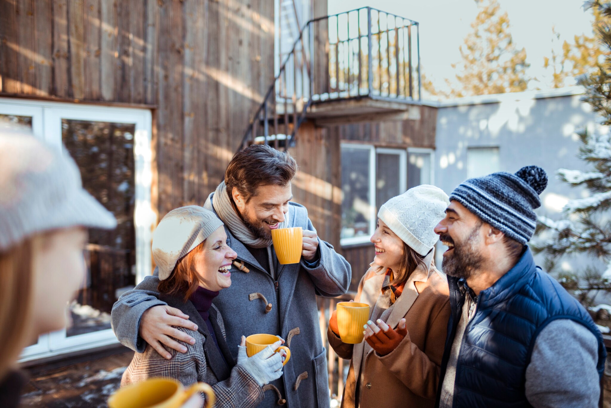 Freunde stehen im Winter vor eine Holzhütte und lachen und reden miteinander