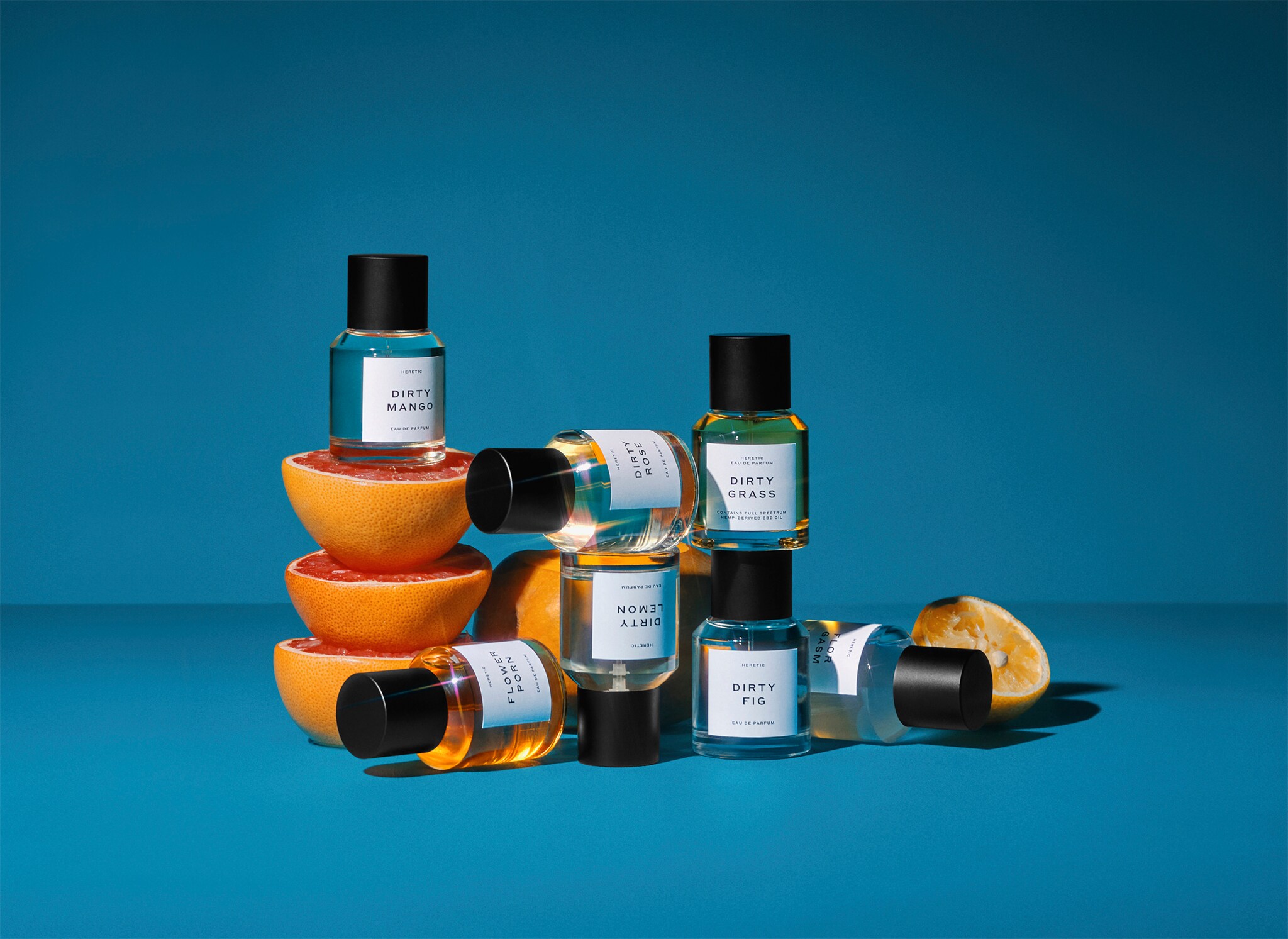 Sieben schlichte Parfümflakons sind vor blauem Hintergrund um Orangenhälften drapiert