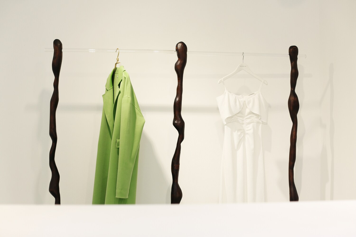 Ein limonengrüner Mantel hängt neben einem weißen Trägerkleid auf einer besonderen Kleiderstange im William-Fan-Store.