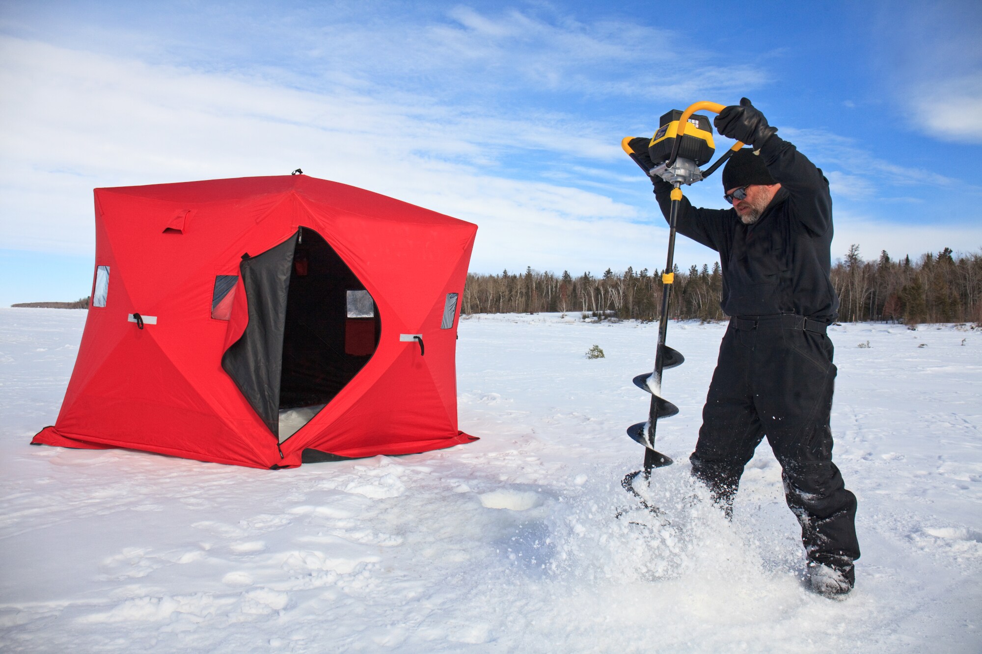 Ein Eisangler bohrt ein Loch in einen zugefrorenen See Ein Eisangler bohrt ein Loch in einen zugefrorenen See